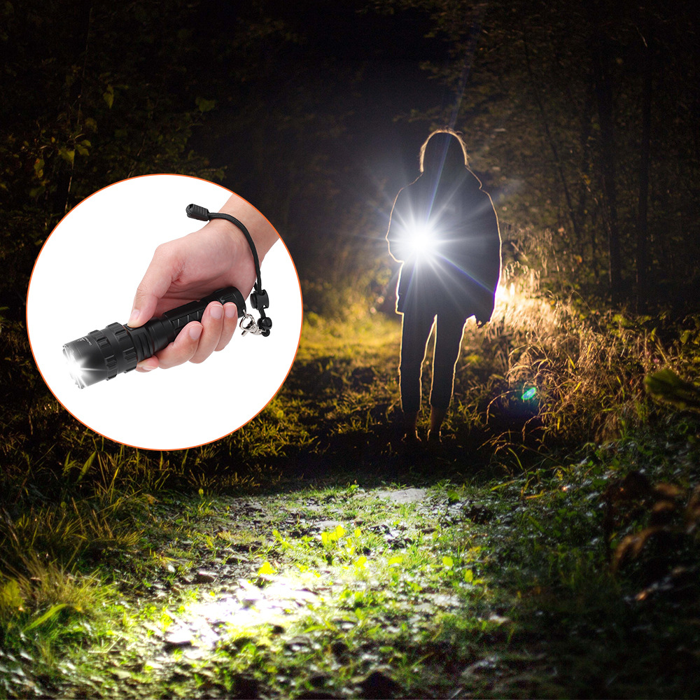 Eine Hand hält eine Taschenlampe, im Hintergrund steht eine Person mit einer leuchtenden Taschenlampe im Wald.