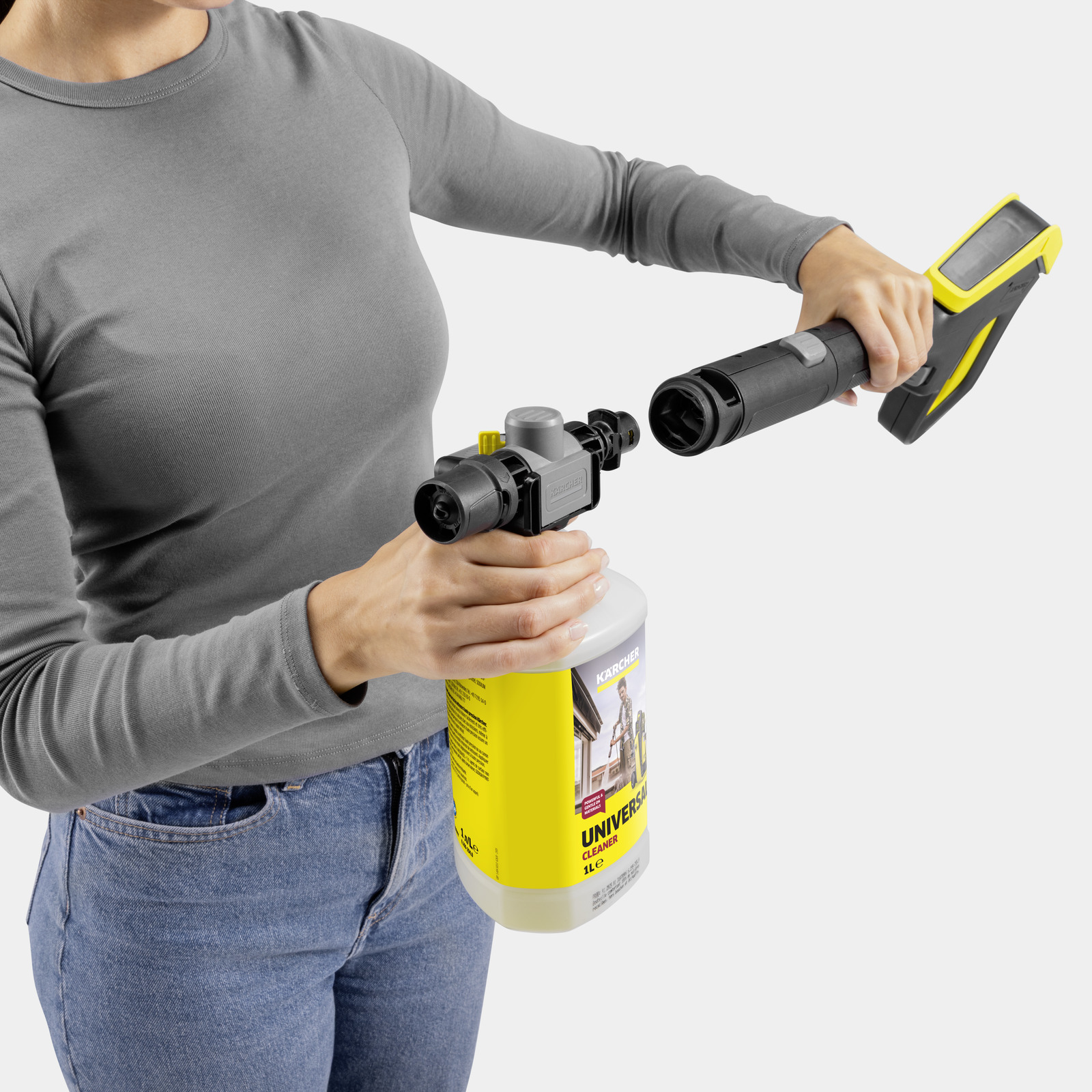 Een persoon in een grijs shirt en spijkerbroek bevestigt een Karcher reinigerfles.