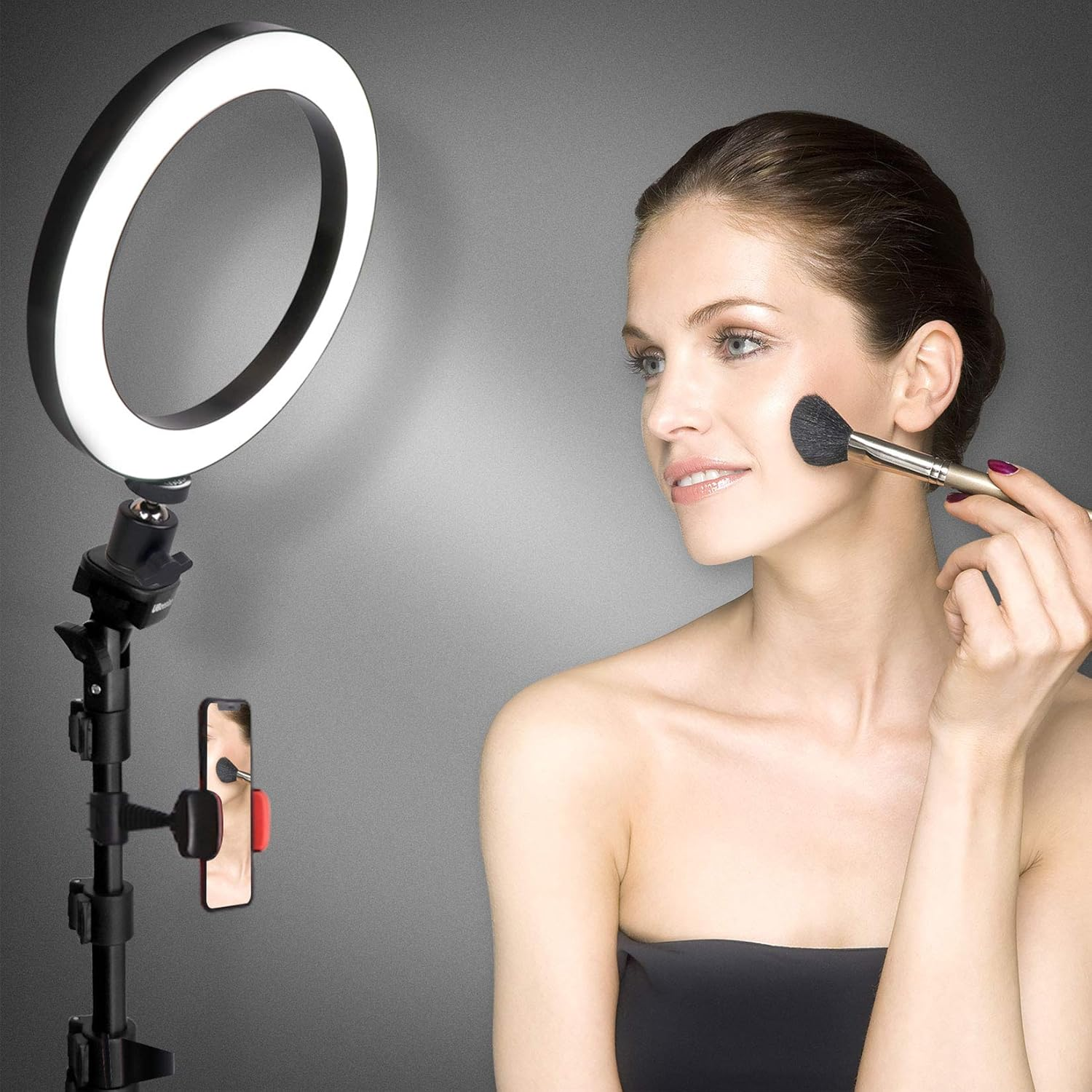 Una donna si trucca, illuminata da un ring light, con uno smartphone su treppiede.