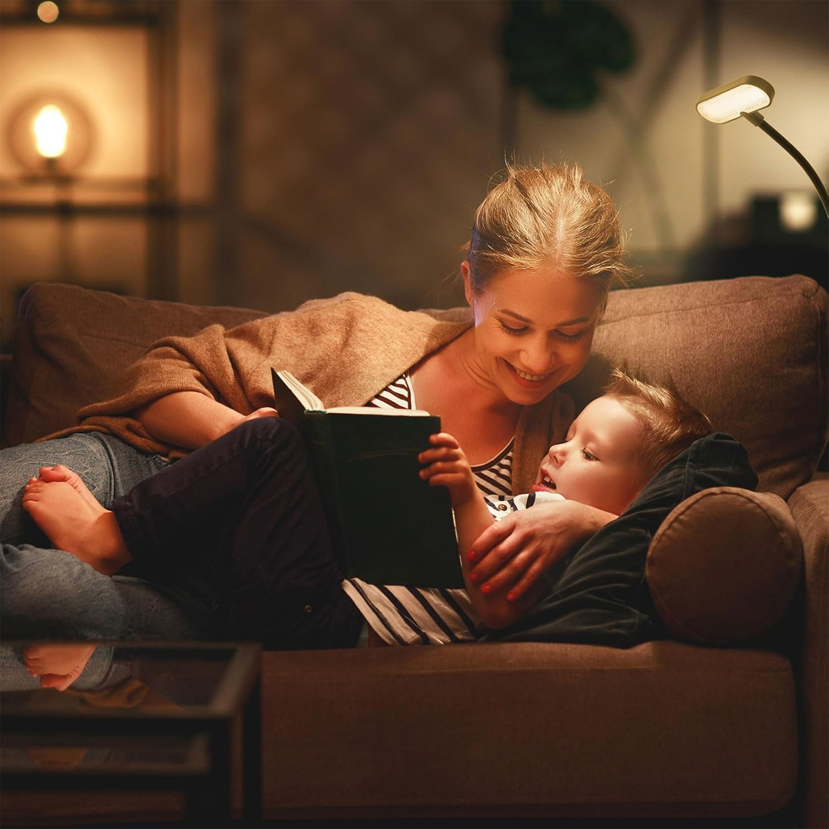 Mutter liest Kind auf Sofa ein Buch vor, beleuchtet von einer Lampe.
