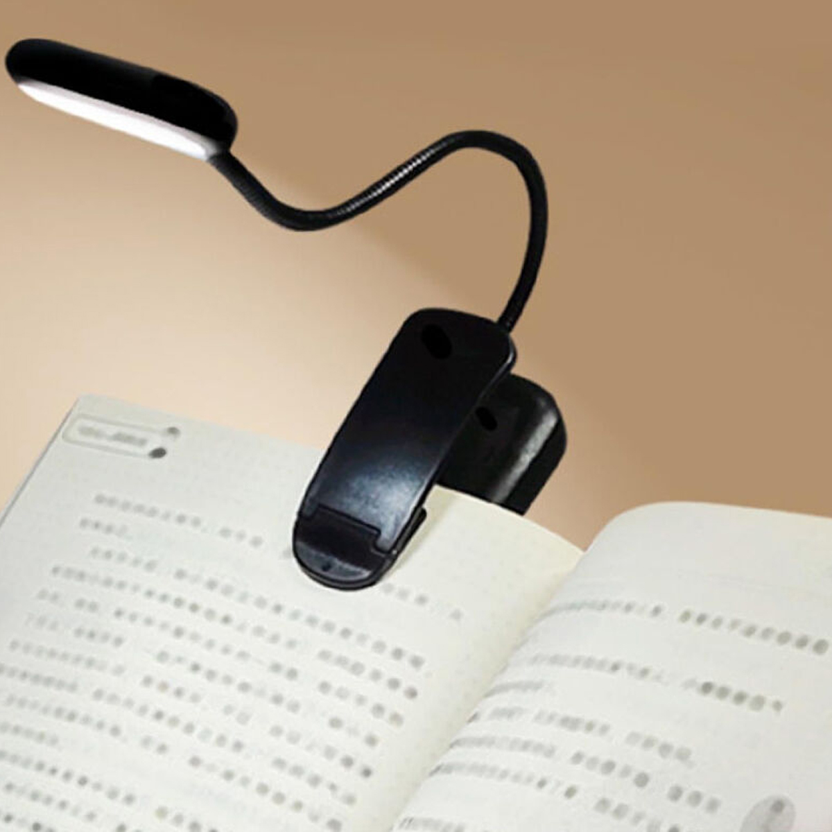 Eine schwarze Klemmleuchte beleuchtet ein offenes Buch mit Text.