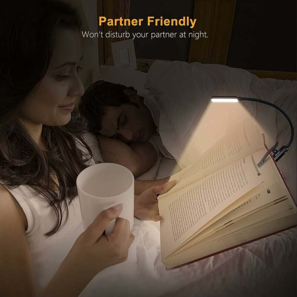 Eine Frau liest im Bett, ein Mann schläft daneben. Ein Buchlicht beleuchtet das Buch.
