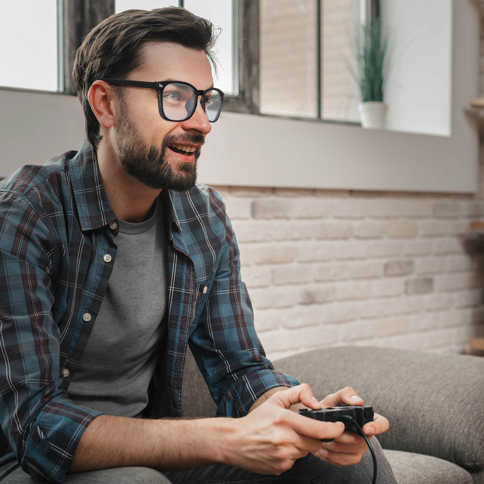 Uomo con occhiali gioca ai videogiochi con controller in soggiorno.