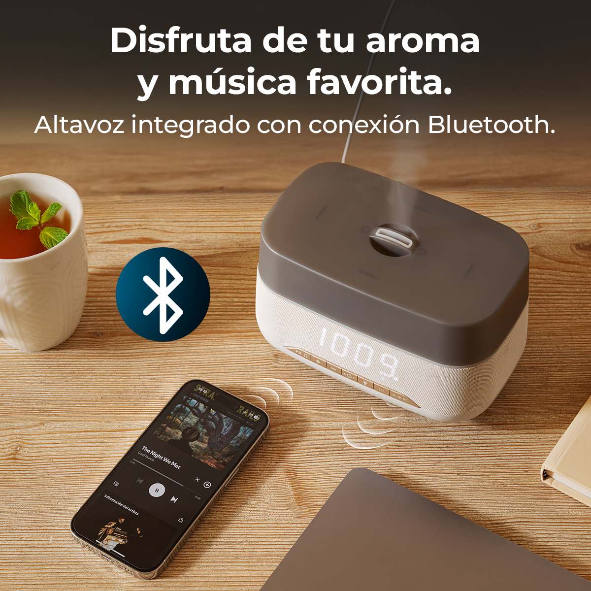 Un altoparlante Bluetooth con tazza da tè, smartphone e libro su tavolo di legno.