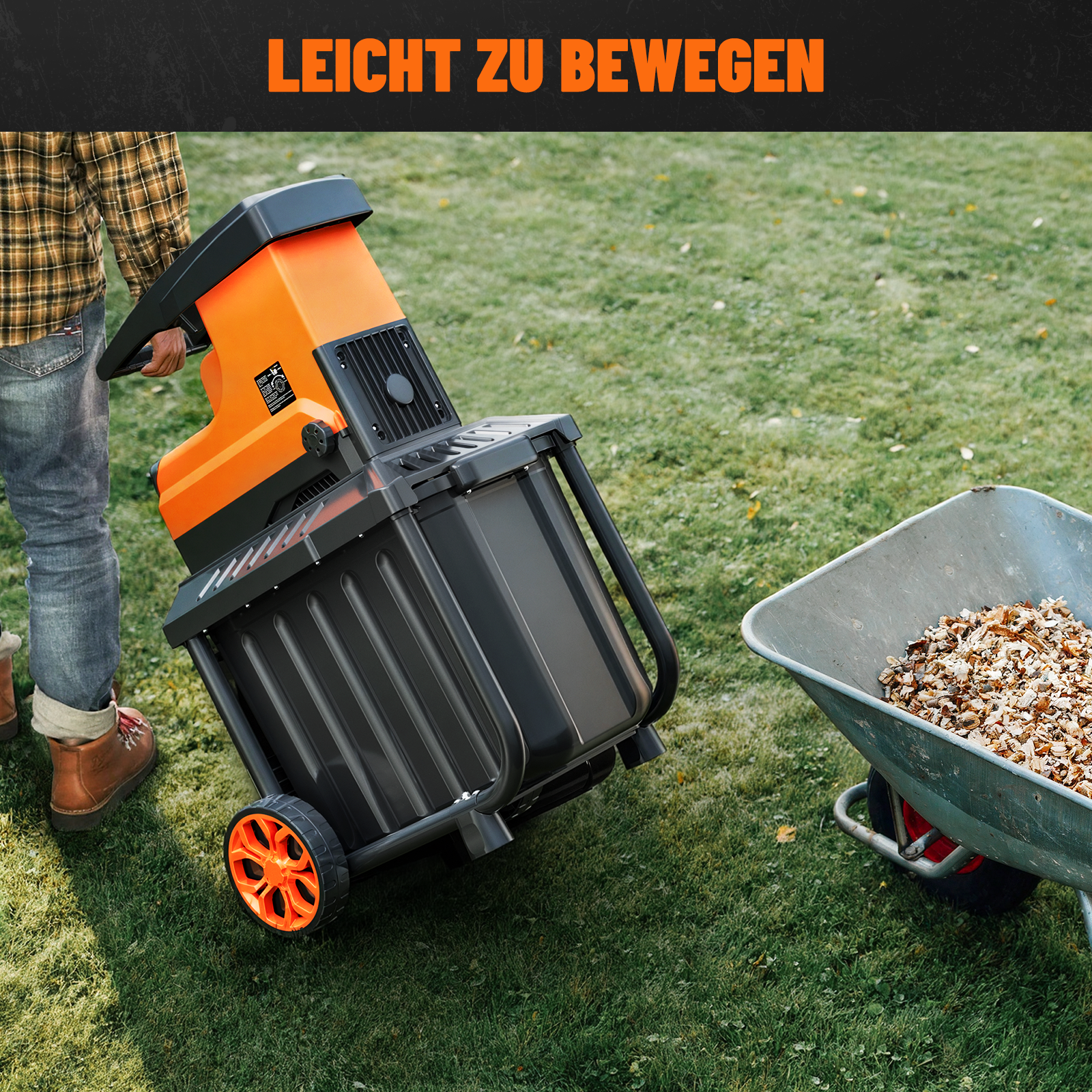 Ein Mann schiebt einen orange-schwarzen Häcksler mit großen Rädern über Gras.