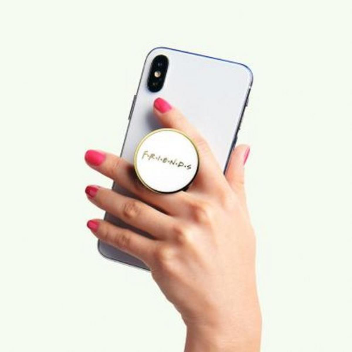 Una mano con uñas rojas sostiene un teléfono inteligente blanco con un clip redondo de "Friends".