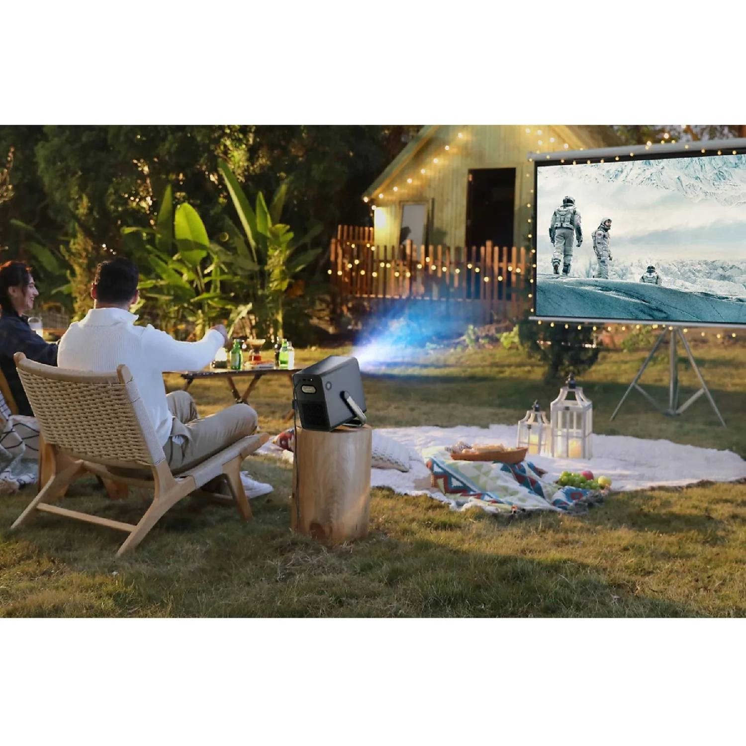 Zwei Personen schauen draußen einen Film auf einer Leinwand, die von einem Projektor beleuchtet wird.