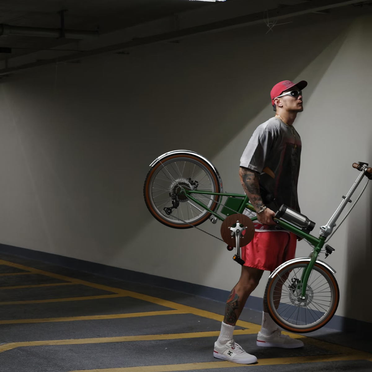 Mężczyzna z wytatuowanymi nogami niesie zielony rower w garażu.