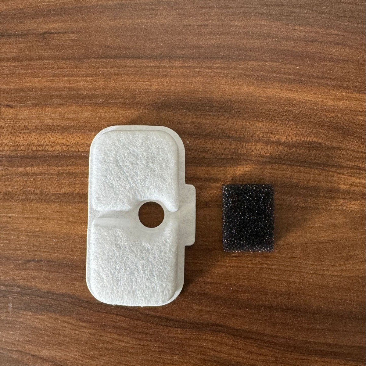 Ein weißer Luftfilter und ein kleiner schwarzer Schaumstofffilter auf Holz.