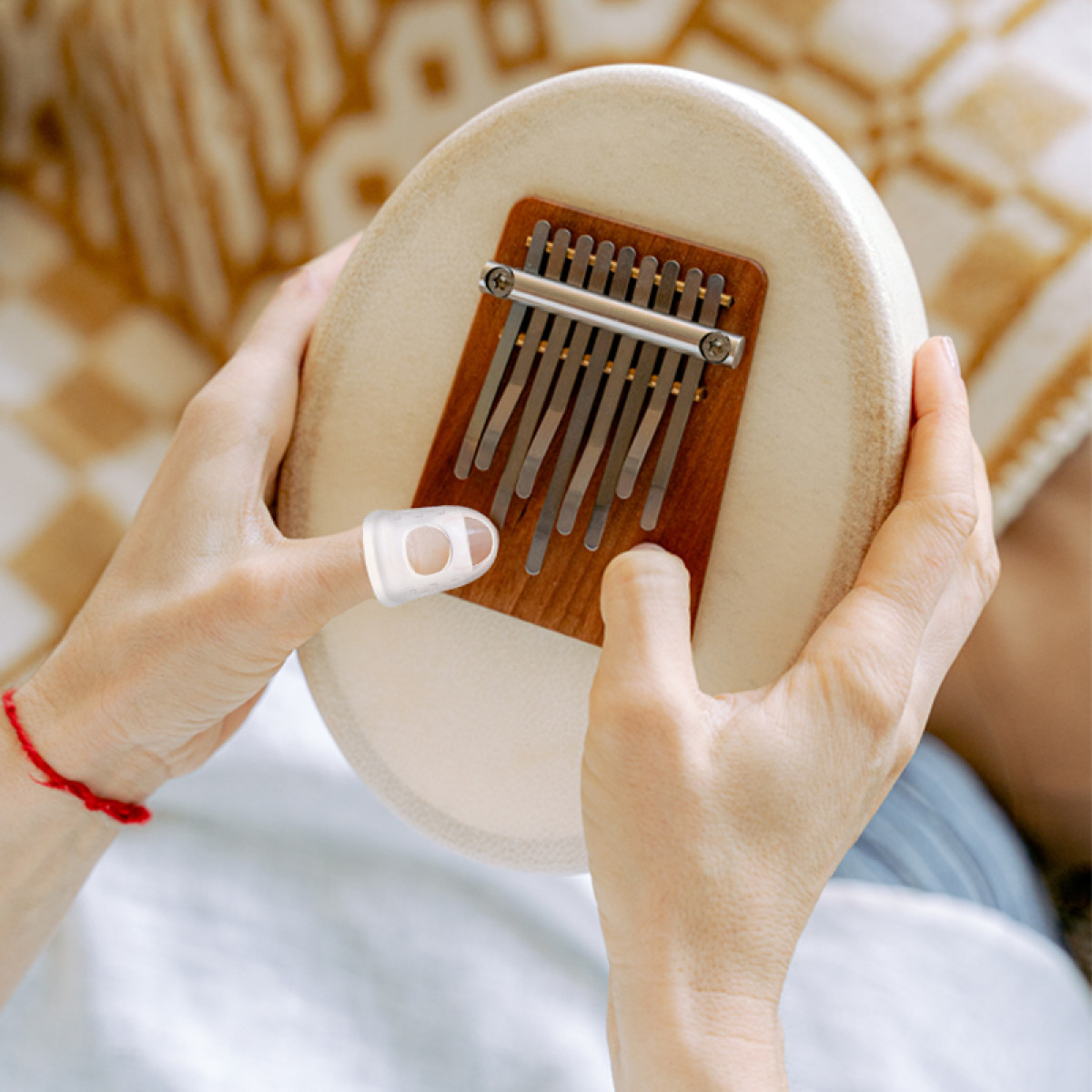 Dłonie grające na kalimbie z ochraniaczem na kciuk na jasnym instrumencie.