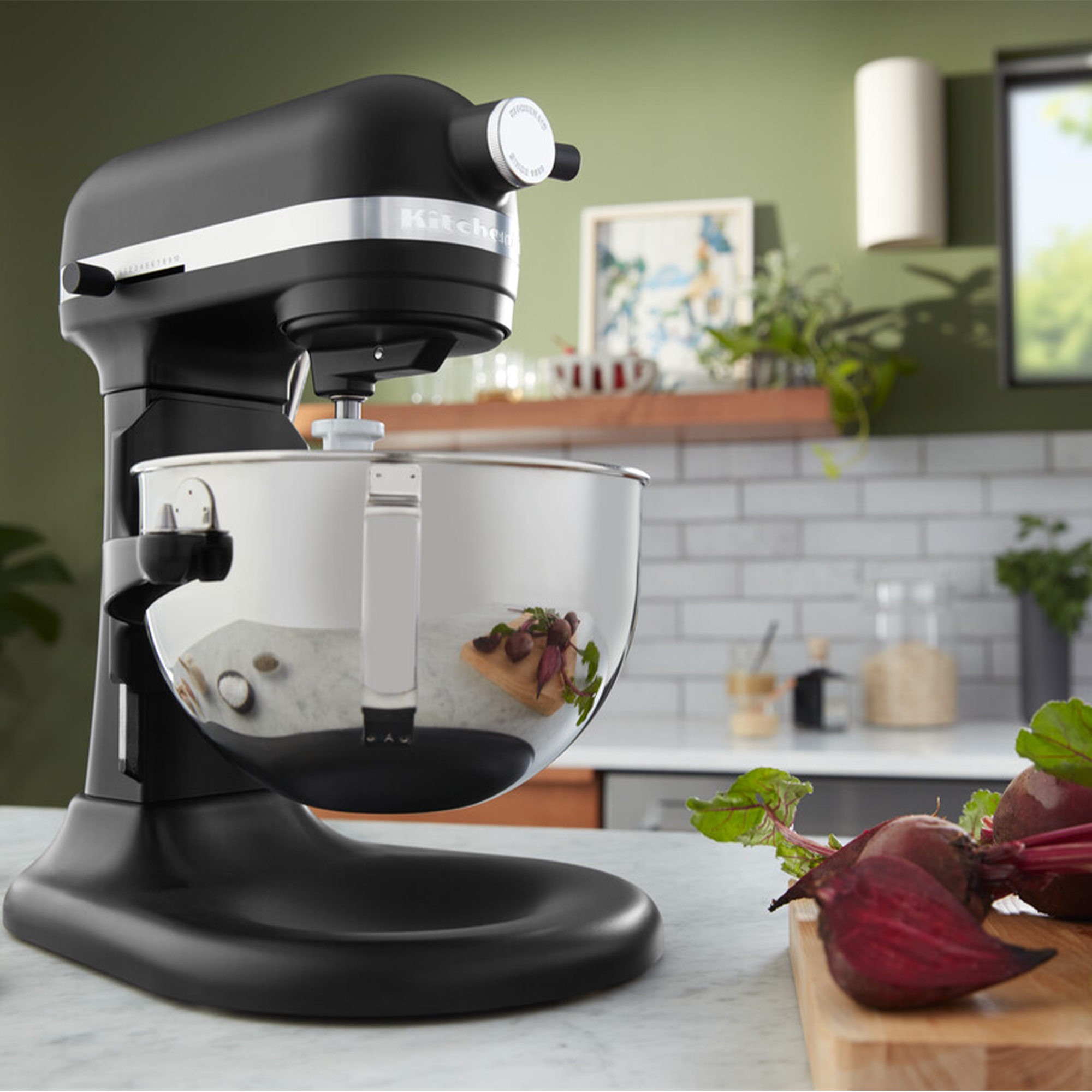 Ein schwarzer Küchenmaschinen-Standmixer mit Edelstahlschüssel und Rote Bete daneben.
