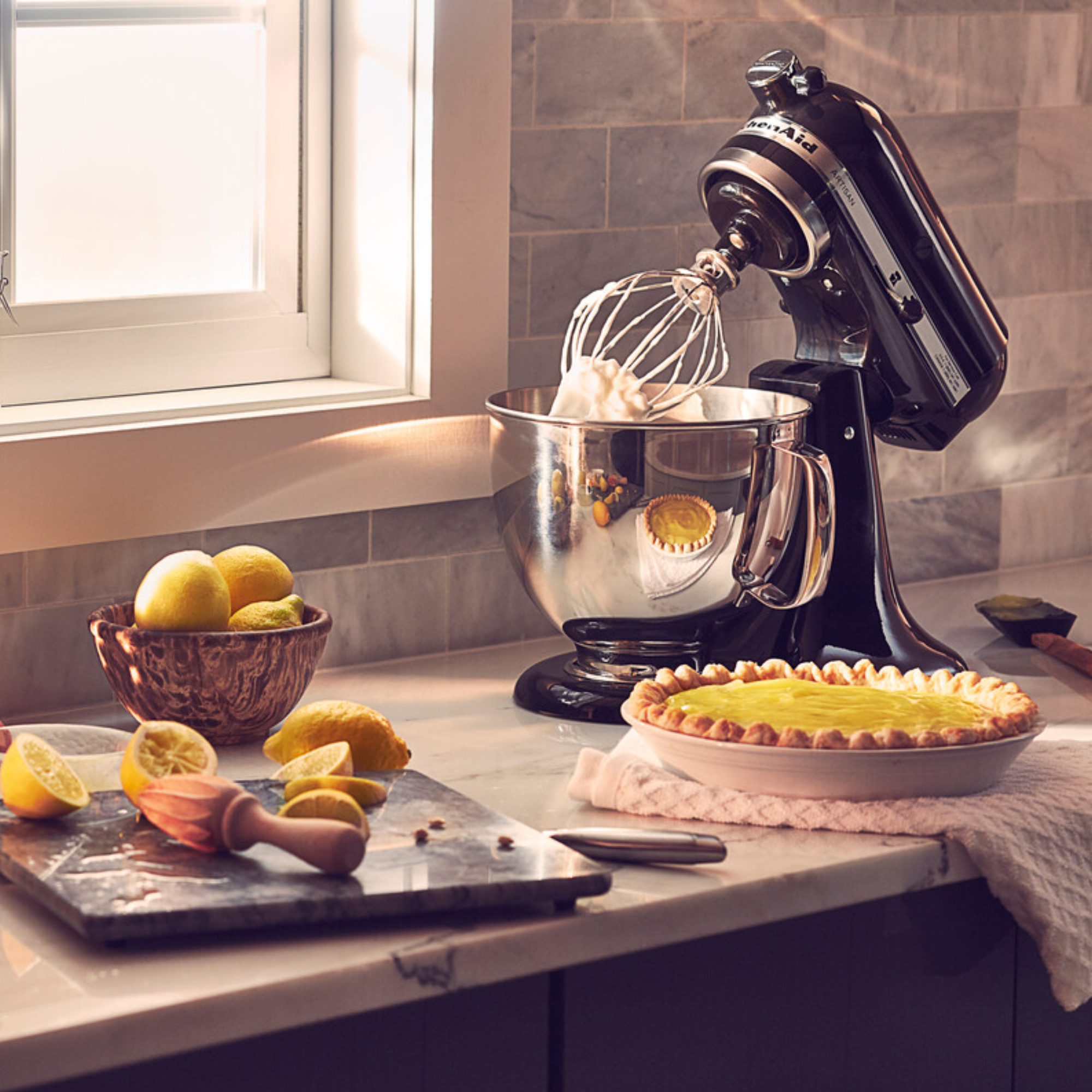 Ein schwarzer Küchenmixer mit Schneebesen, der Sahne schlägt, neben einem Zitronenkuchen.