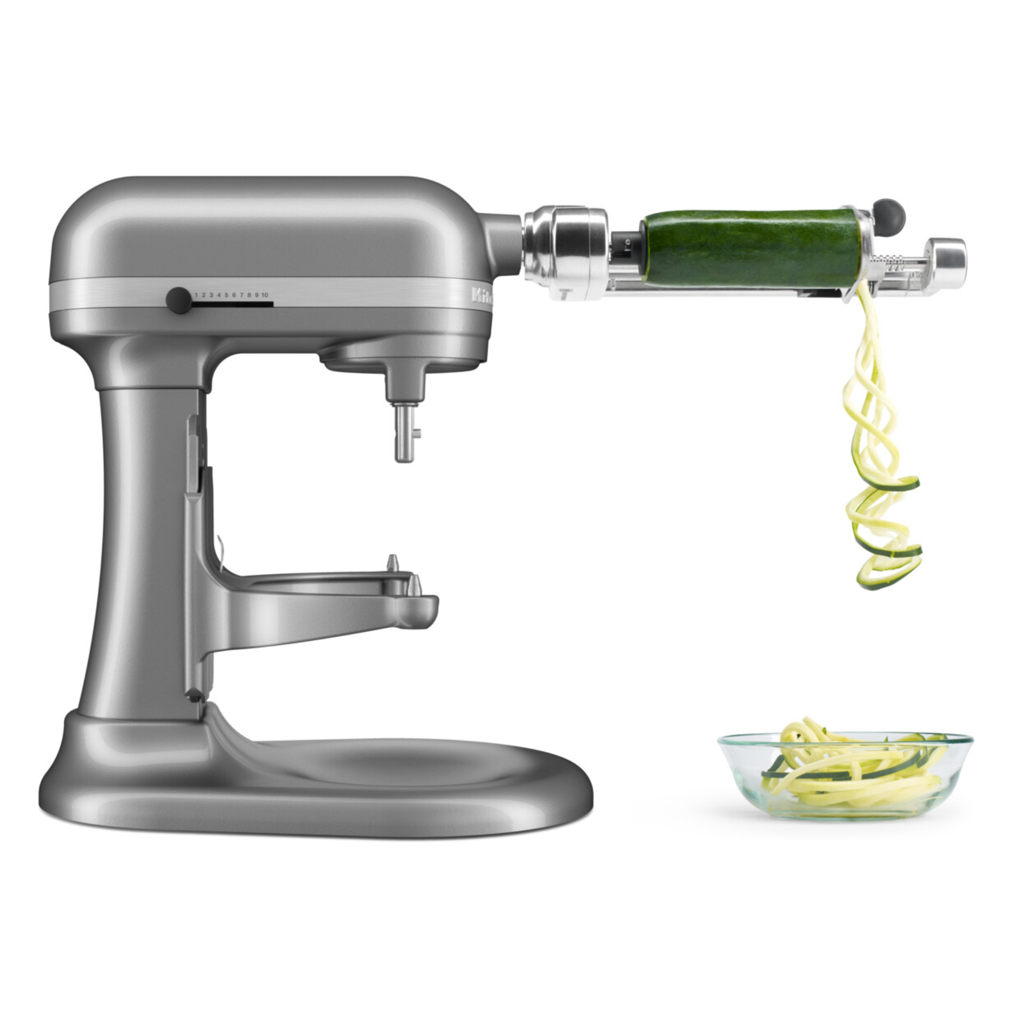 Ein silberner Küchenmaschinenaufsatz schneidet eine Zucchini in Spiralen in eine Schüssel.