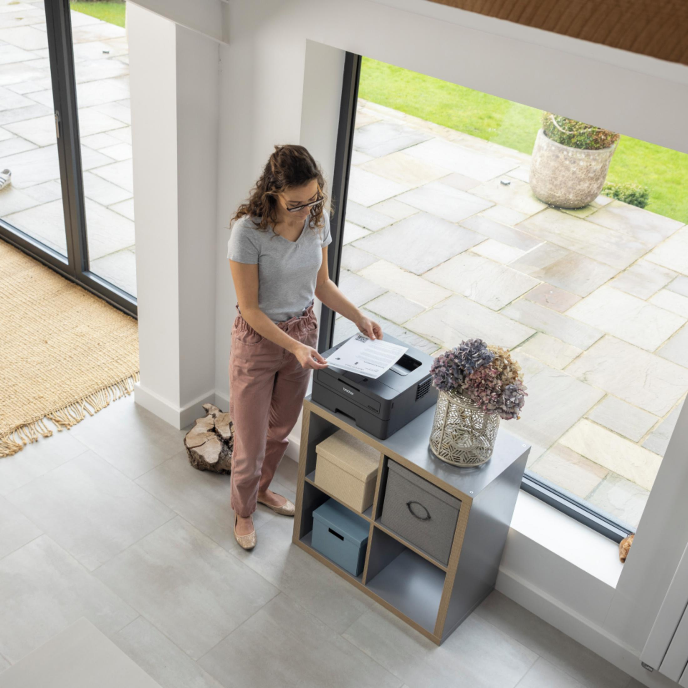 Kobieta z kręconymi włosami i okularami wyjmuje dokument z drukarki.