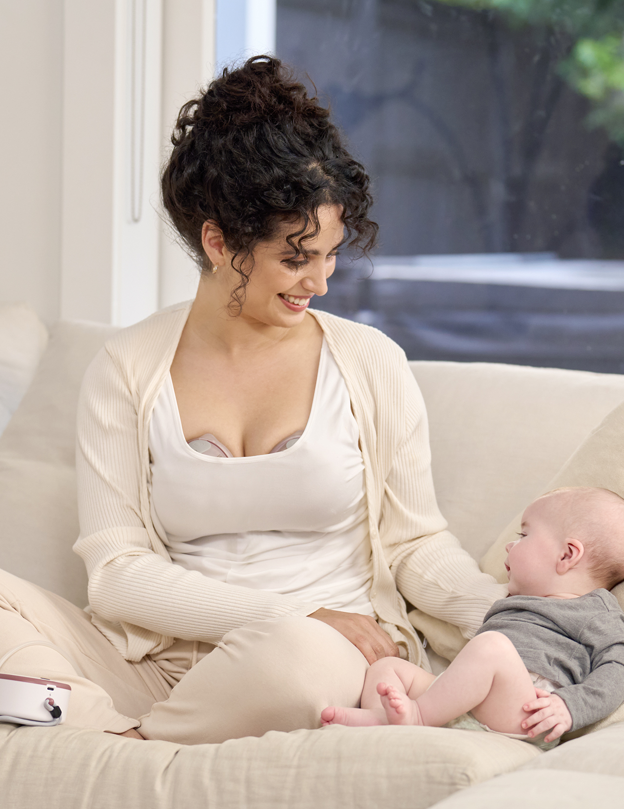 Eine Frau mit dunklen, lockigen Haaren sitzt auf einer Couch und schaut ein Baby an.