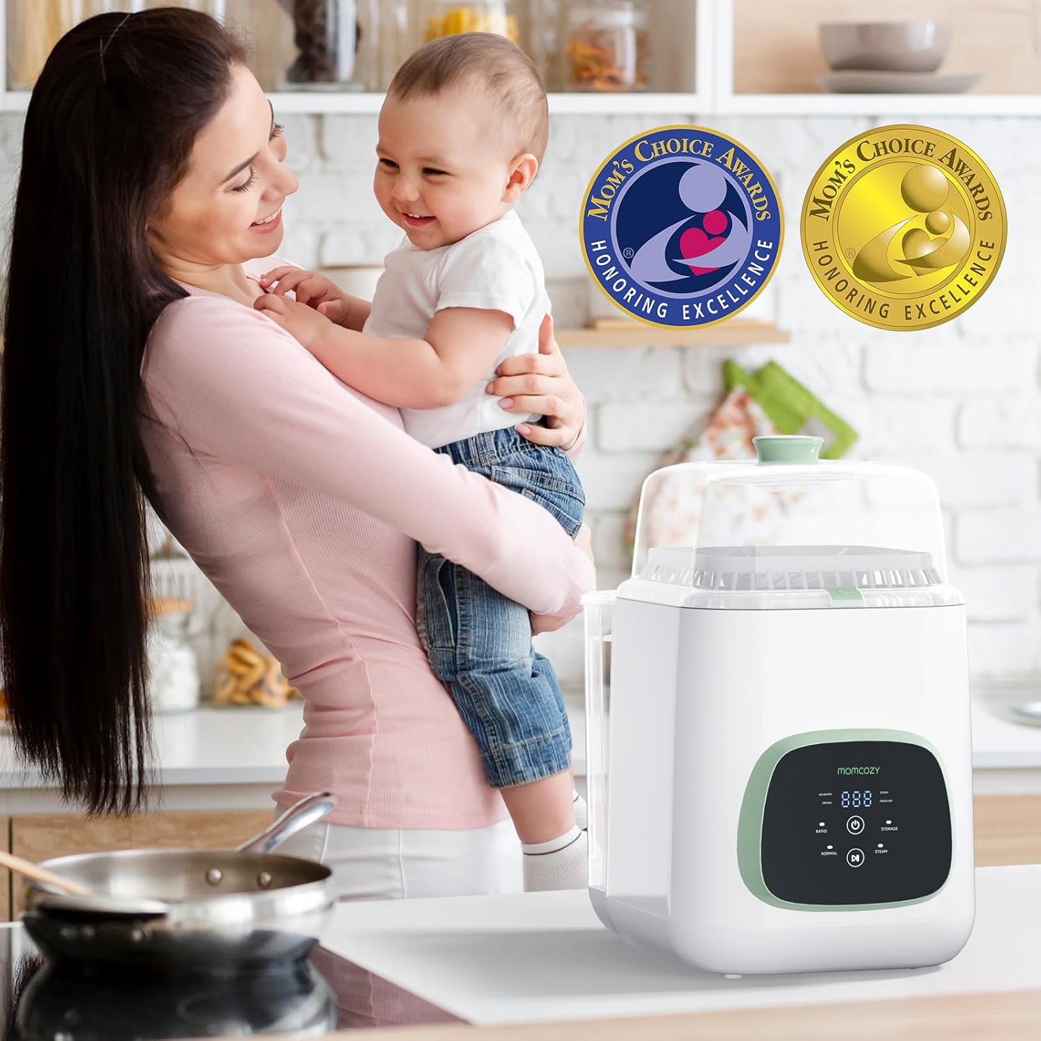Mutter hält lächelndes Baby. Dampfgarer & Mom's Choice Awards im Hintergrund.