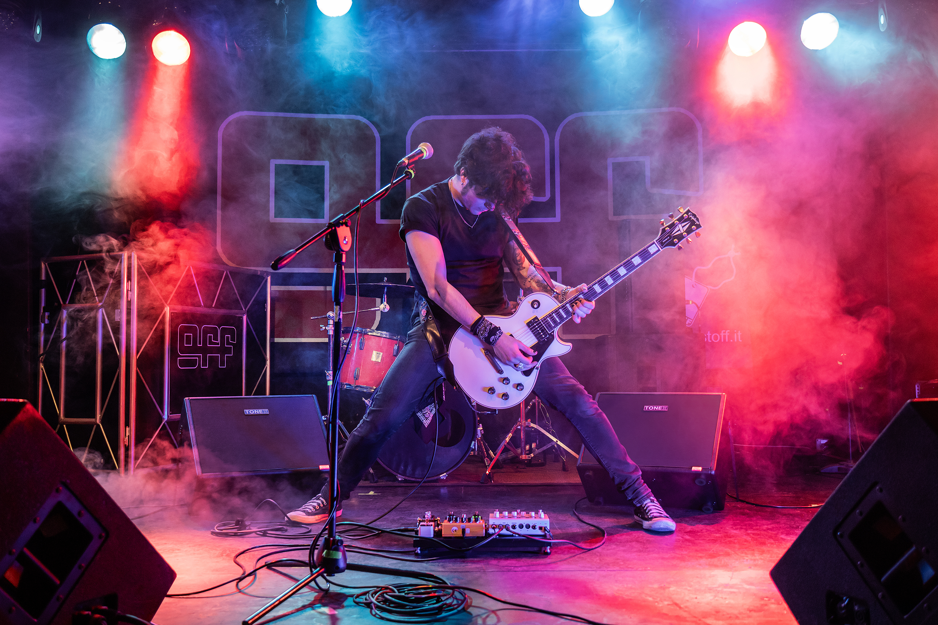 Ein Gitarrist spielt auf einer weißen E-Gitarre im Scheinwerferlicht mit Rauch.
