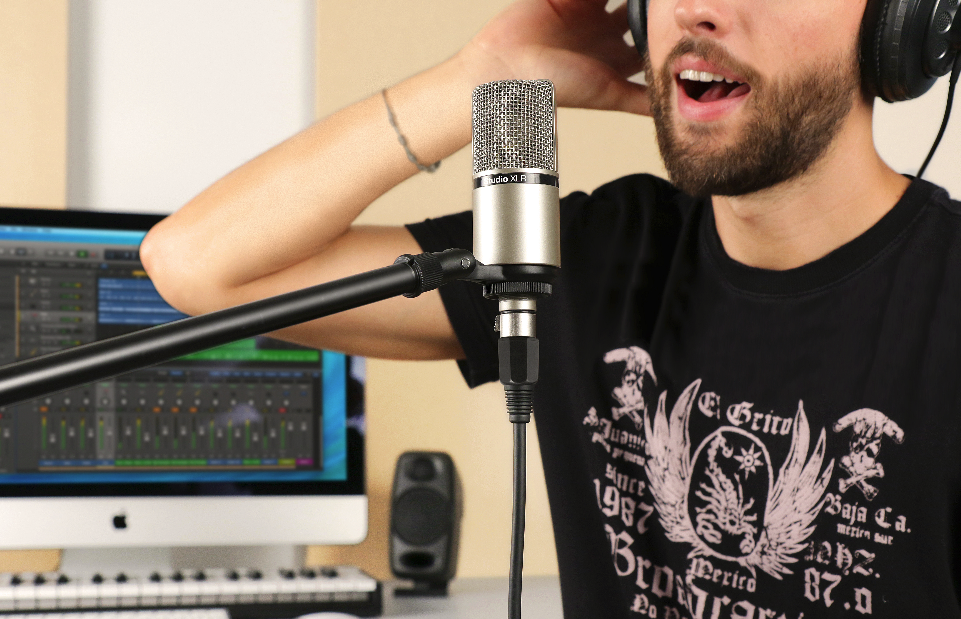Mann mit Kopfhörern singt in ein Mikrofon vor einem Computer mit Aufnahmesoftware.