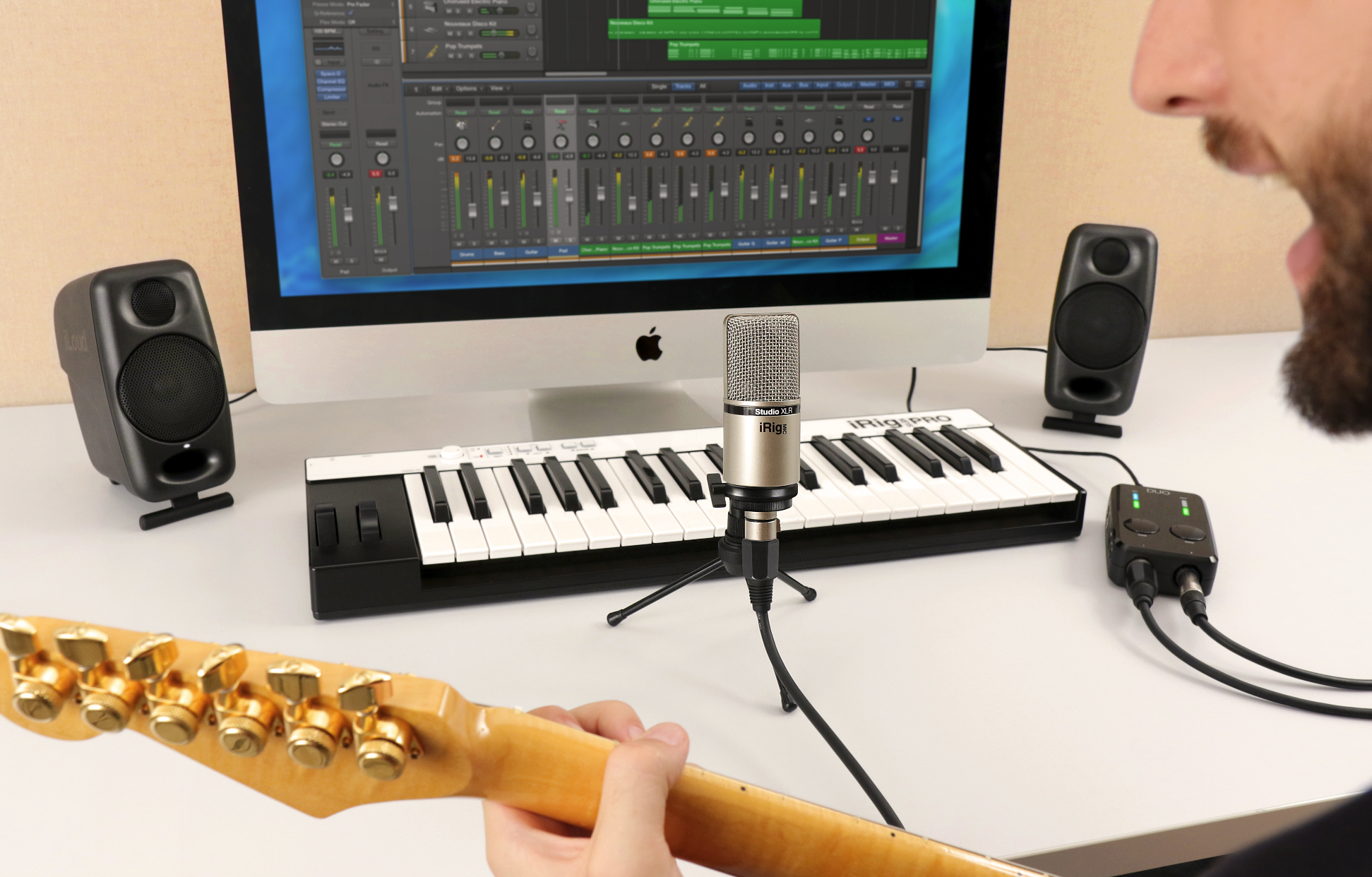 Ein Mann spielt Gitarre vor einem Computer mit Aufnahmesoftware, Mikrofon und Tastatur.