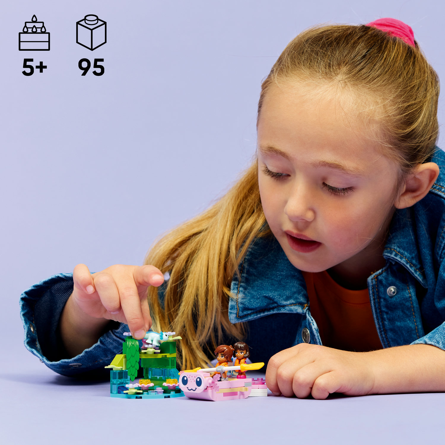 Mädchen spielt mit bunten Lego-Tieren und Figuren auf einem grünen und blauen Bauwerk.