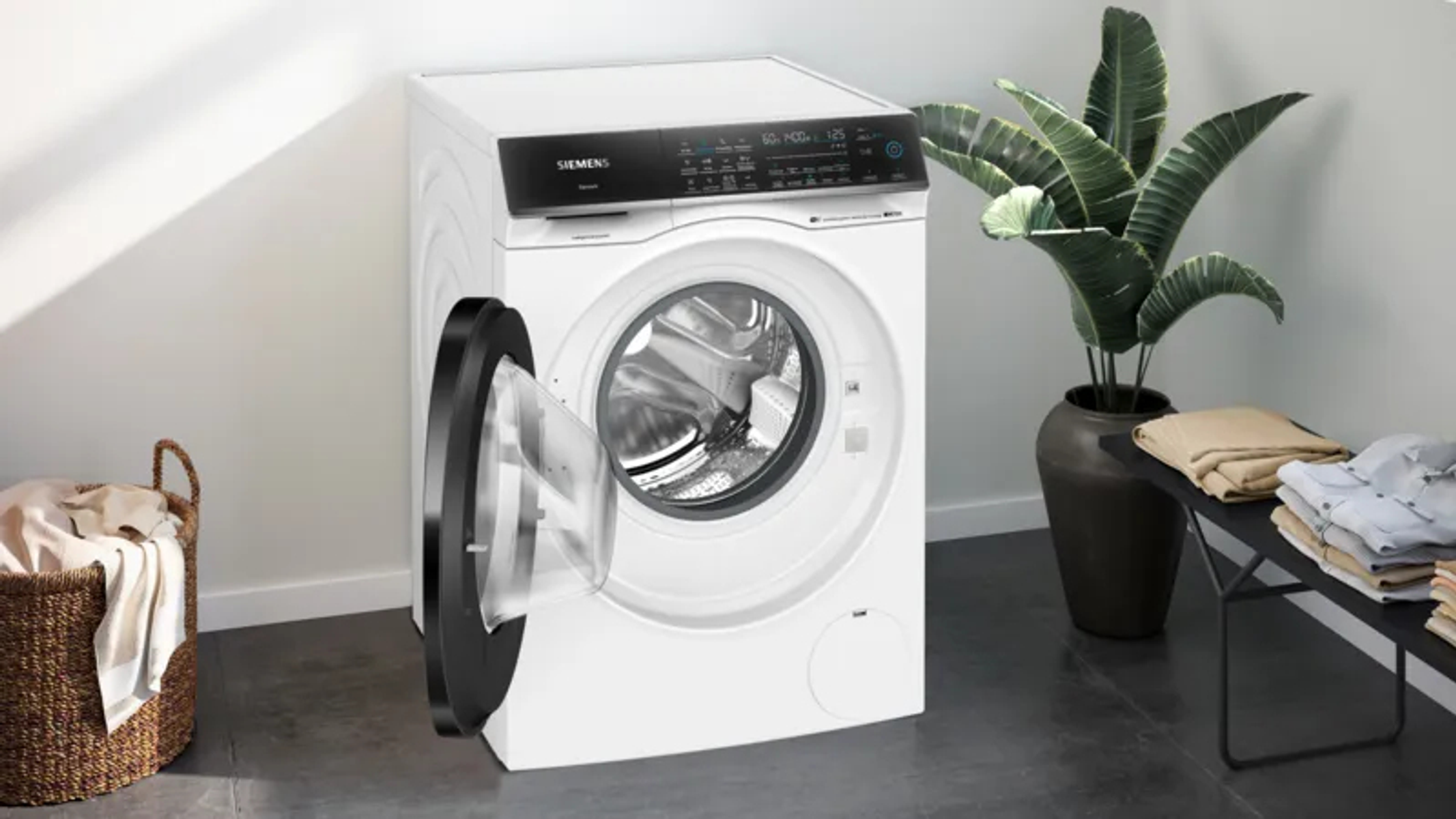 Eine weiße Siemens Waschmaschine mit offener Tür steht neben einem Wäschekorb.