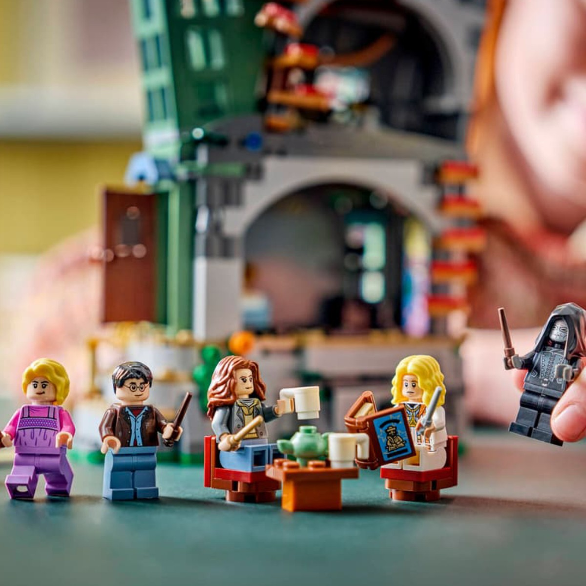 Pięć figurek Lego pije herbatę przed budynkiem. Jedna figurka trzyma książkę.