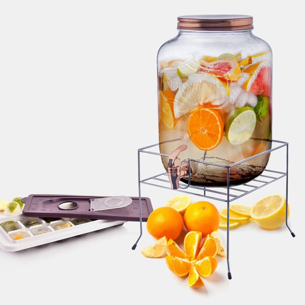 Un dispensador de bebidas de vidrio con fruta y una cubitera.