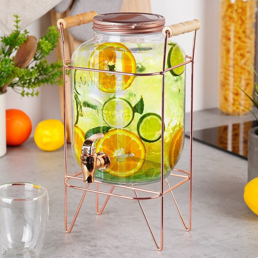 Un dispensador de bebidas de vidrio con naranjas y limas en un soporte de cobre.