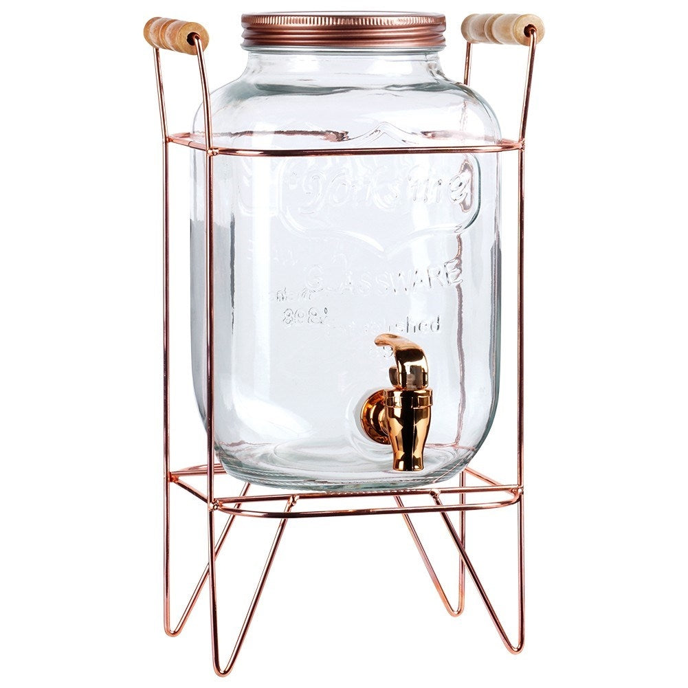 Dispensador de bebidas de vidrio transparente con grifo de cobre y soporte.