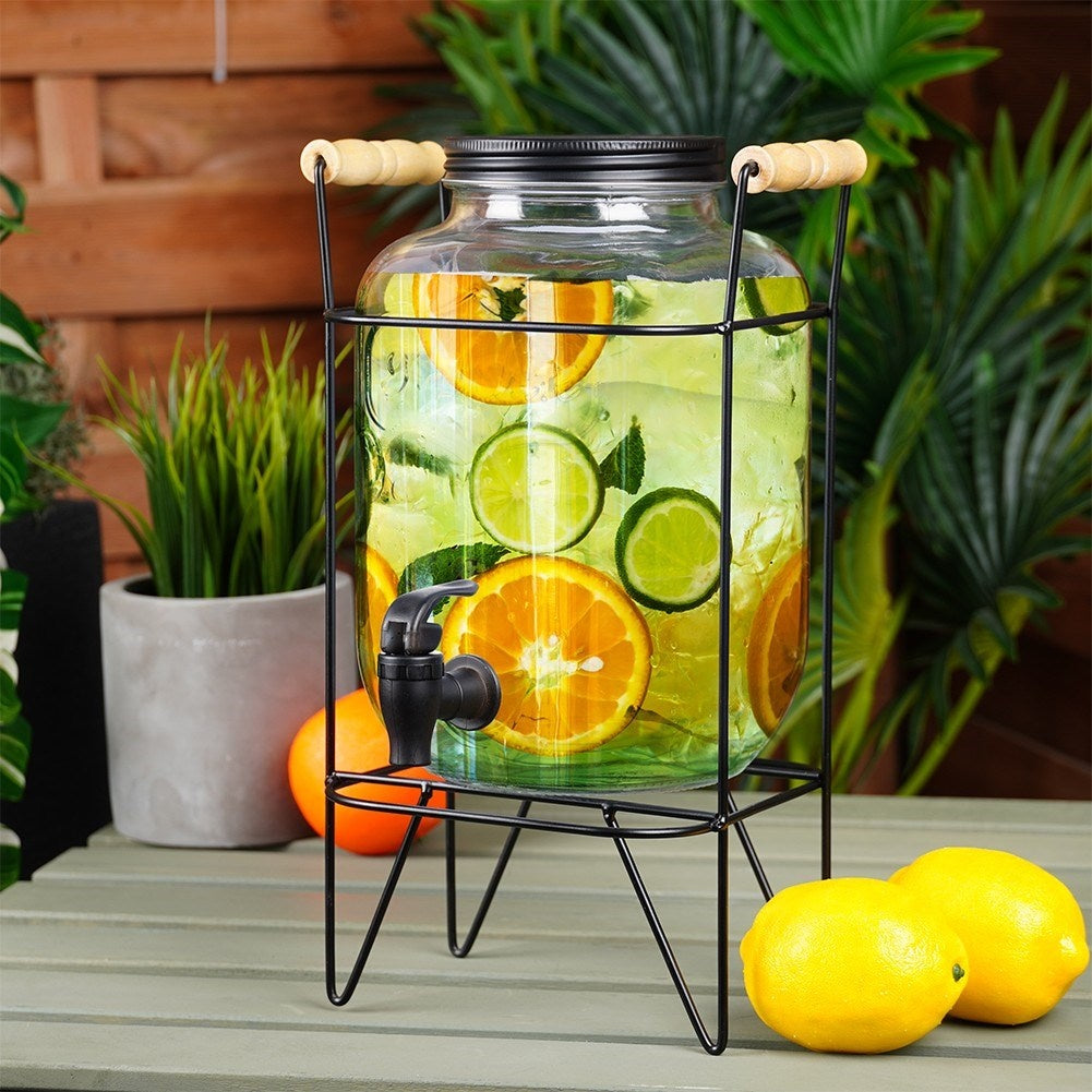 Un dispensador de bebidas con rodajas de naranja y lima, dos limones al lado.