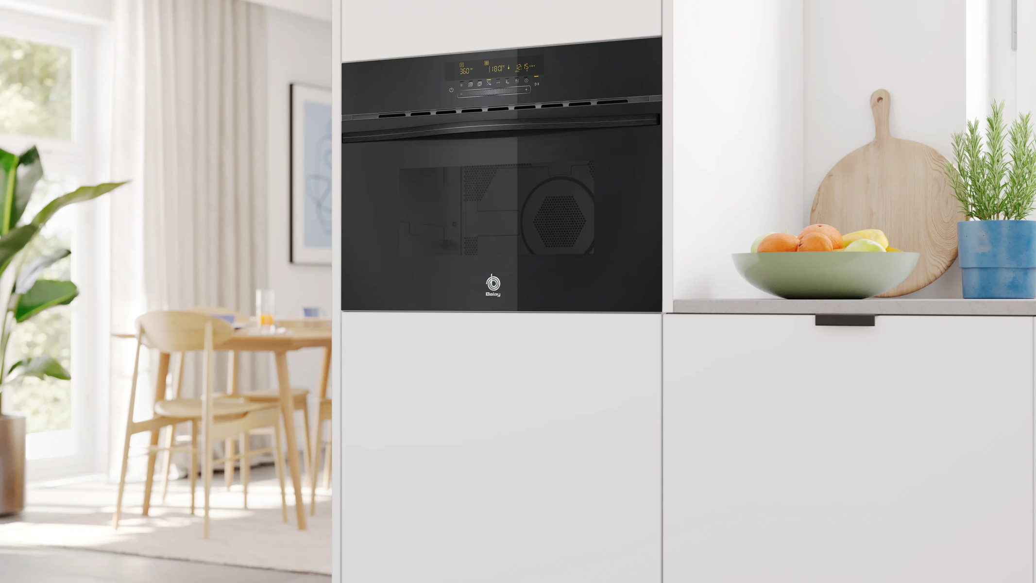 Un horno negro moderno sobre armarios blancos, con un frutero al lado.