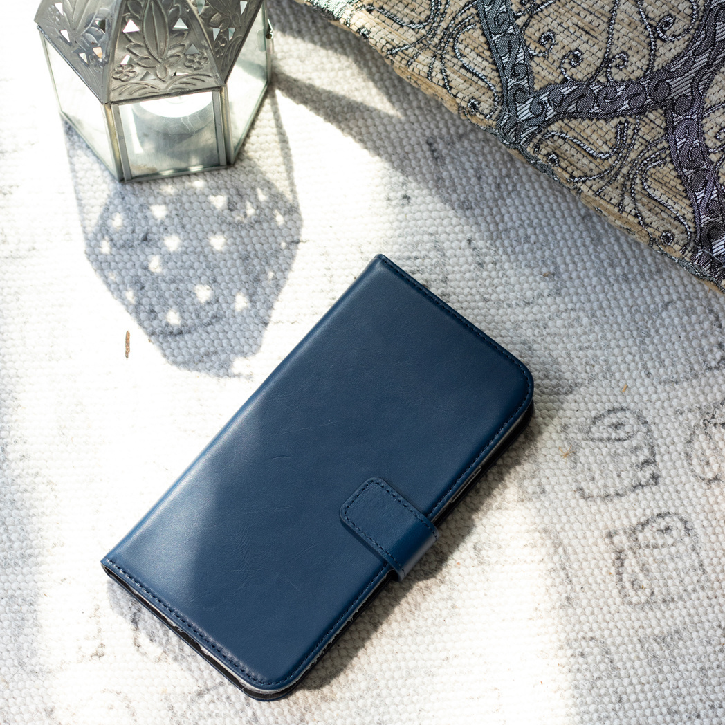 Un étui de téléphone bleu marine fermé repose sur un tapis texturé à côté d'une lanterne.