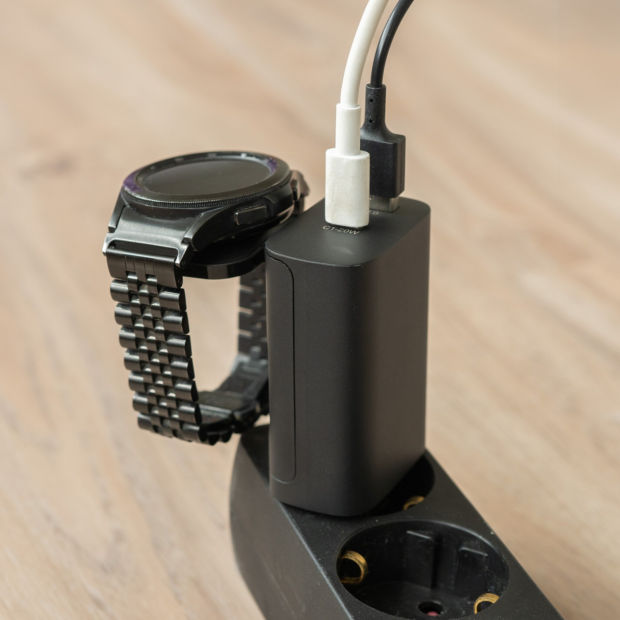 Eine schwarze Smartwatch lädt an einem Netzteil mit zwei Kabeln.