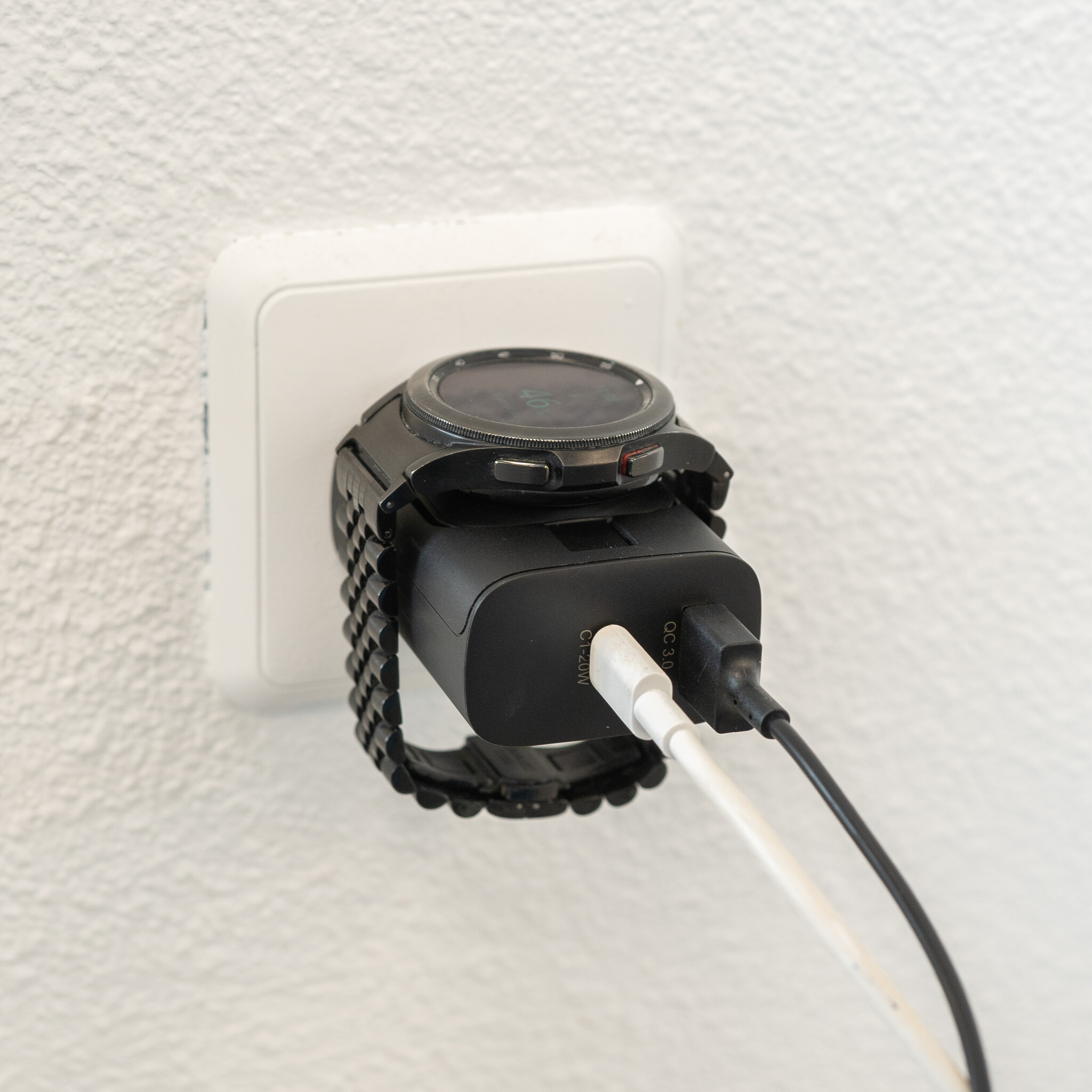 Eine schwarze Smartwatch wird über ein Ladekabel an eine weiße Steckdose angeschlossen.