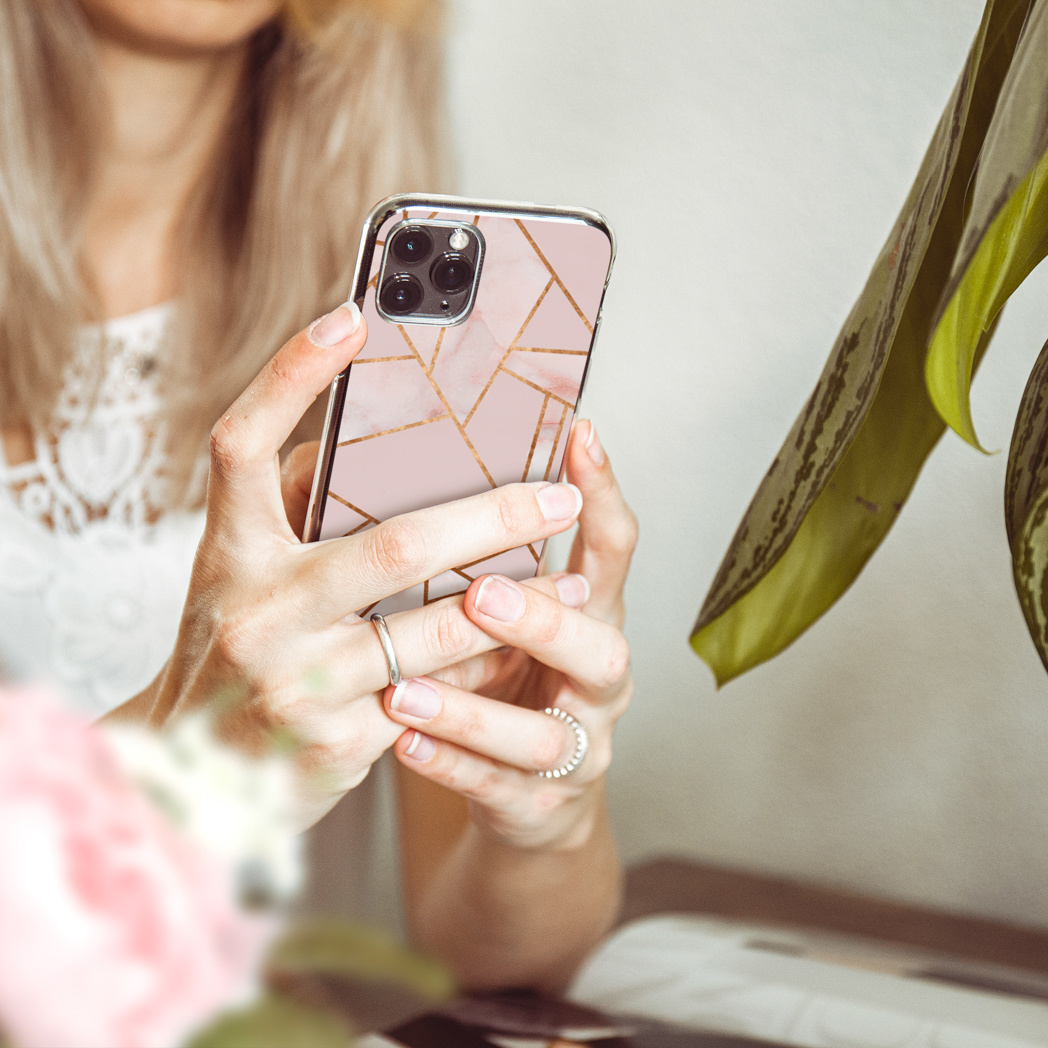 Donna tiene telefono rosa con motivo marmo e linee oro. Primo piano.