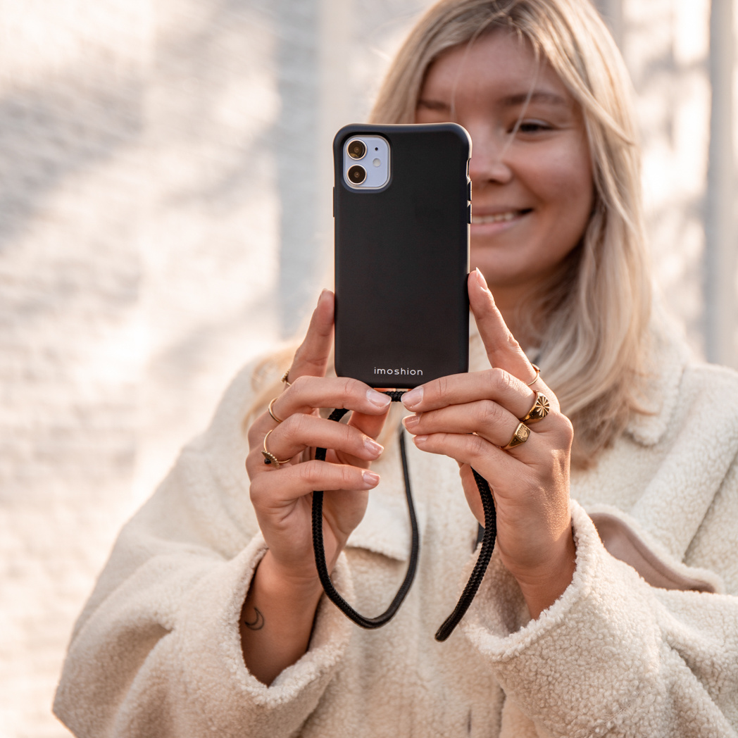 Blondine houdt zwarte telefoon met koord vast. Ze draagt een crèmekleurige jas.