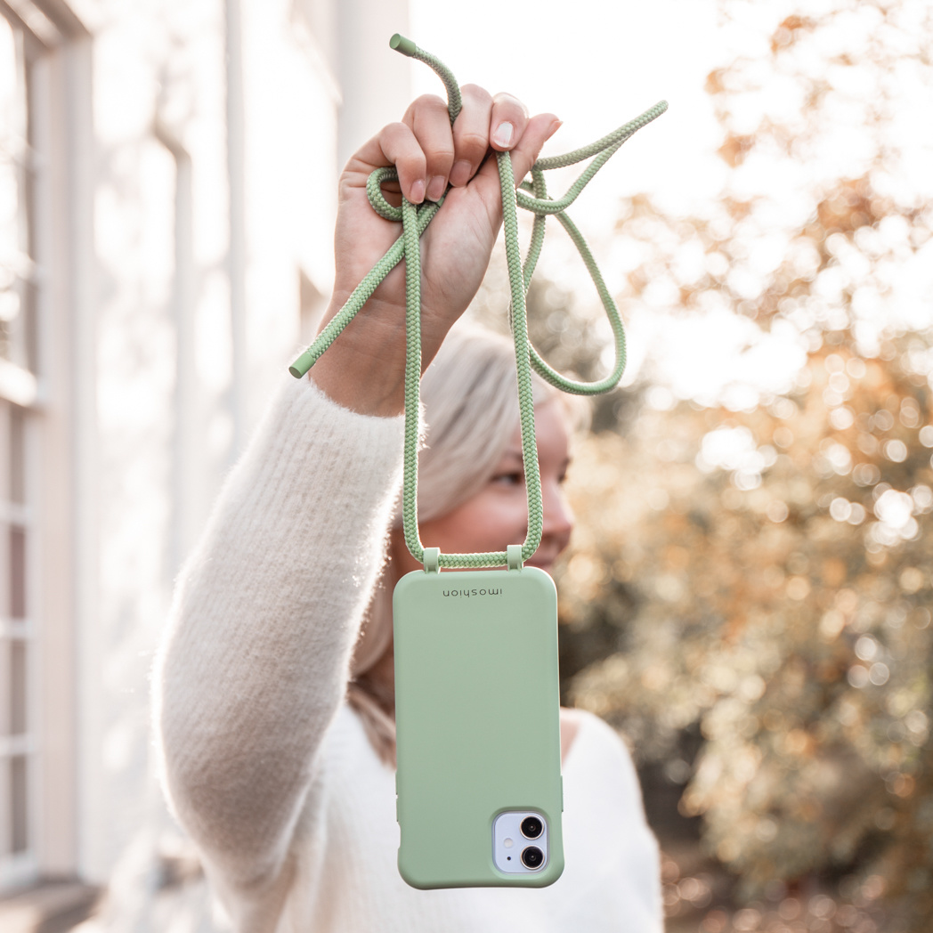 Een persoon houdt een lichtgroene telefoonhoes met band vast.