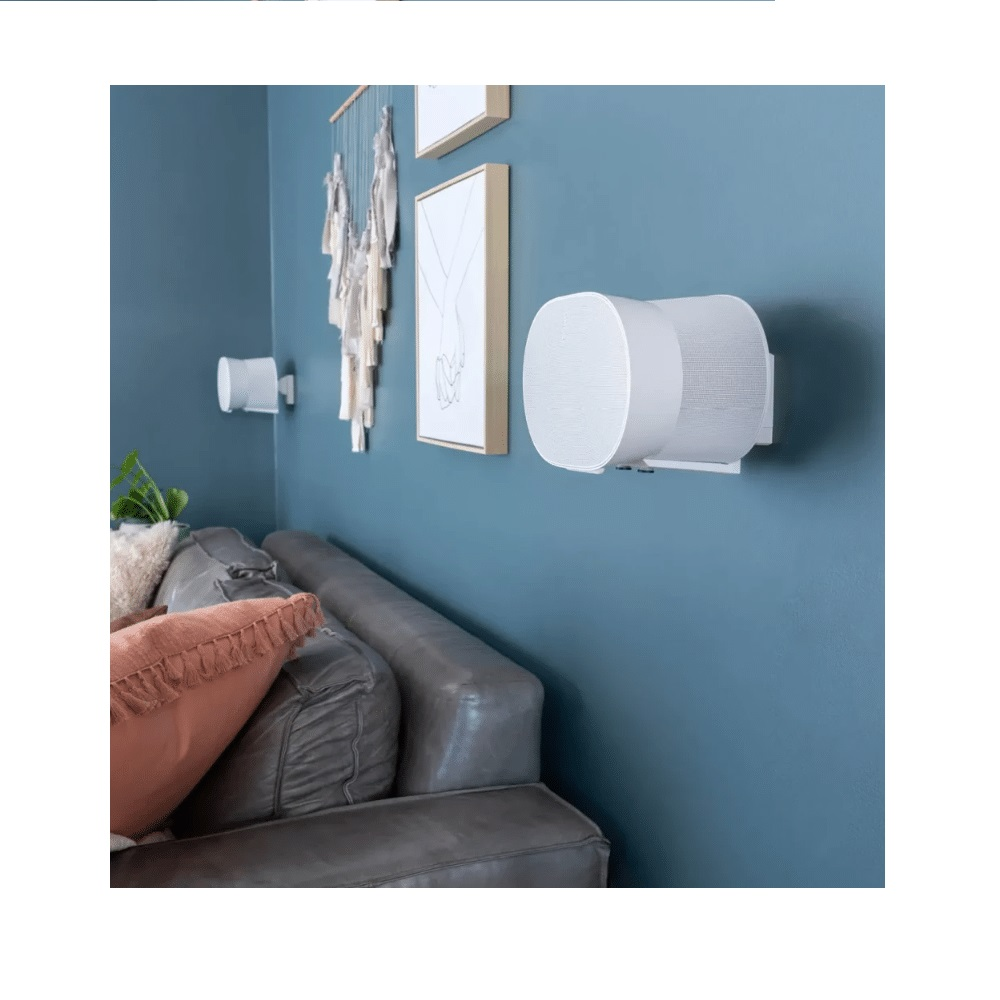 White speakers on blue wall above grey sofa with pillows.