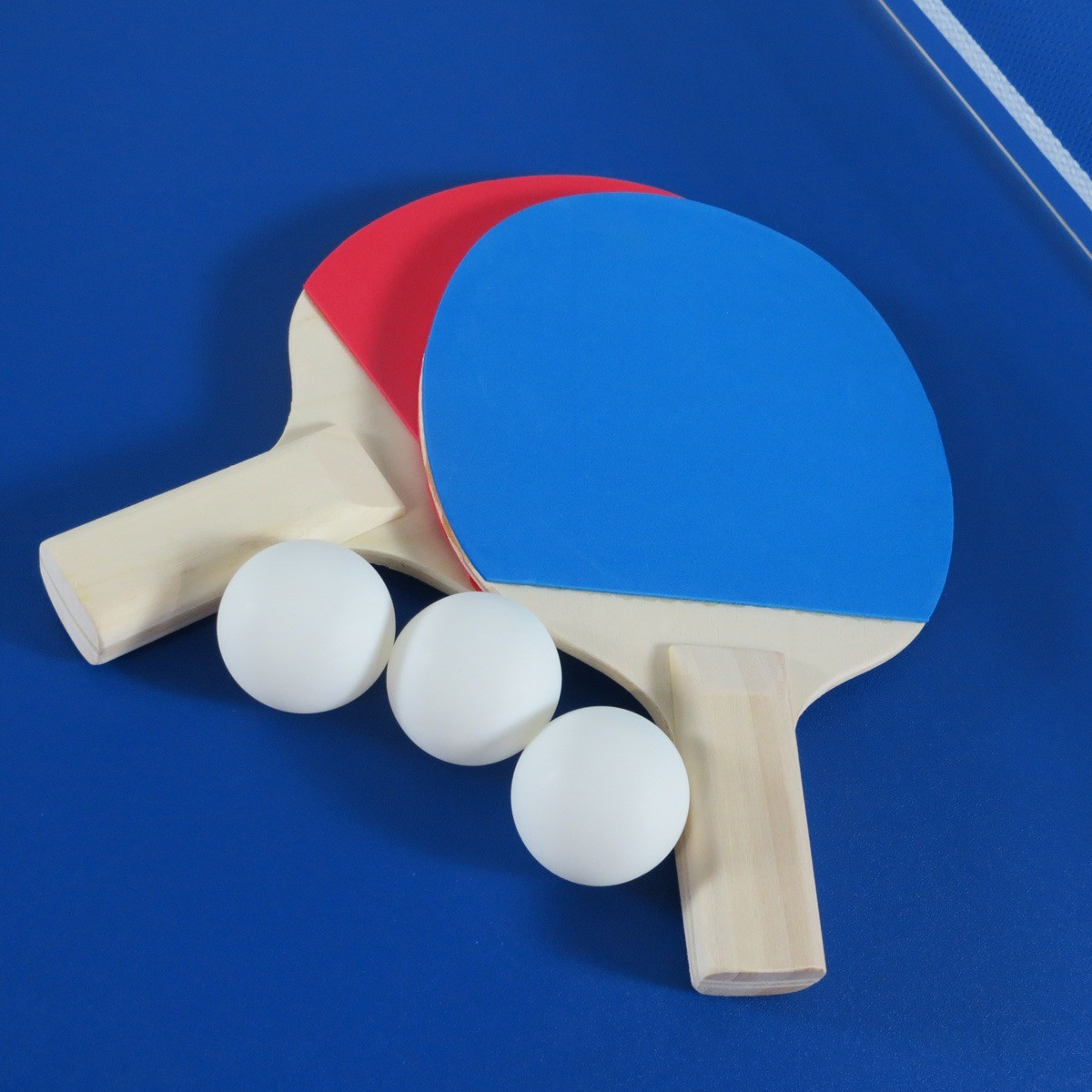 Twee tafeltennisrackets, één blauw, één rood, met drie witte ballen op blauwe tafel.