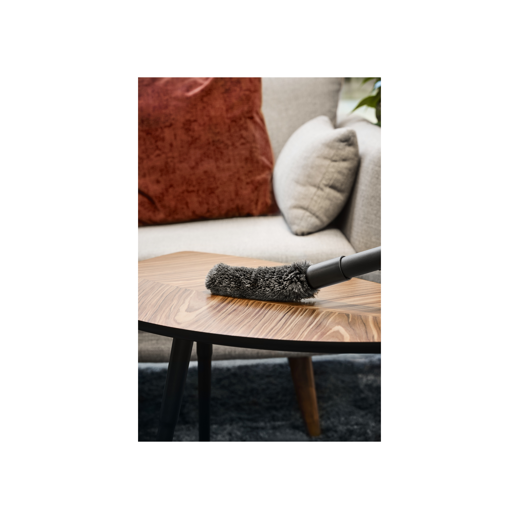 Un accesorio de aspiradora sobre una mesa de madera frente a un sofá con cojines.