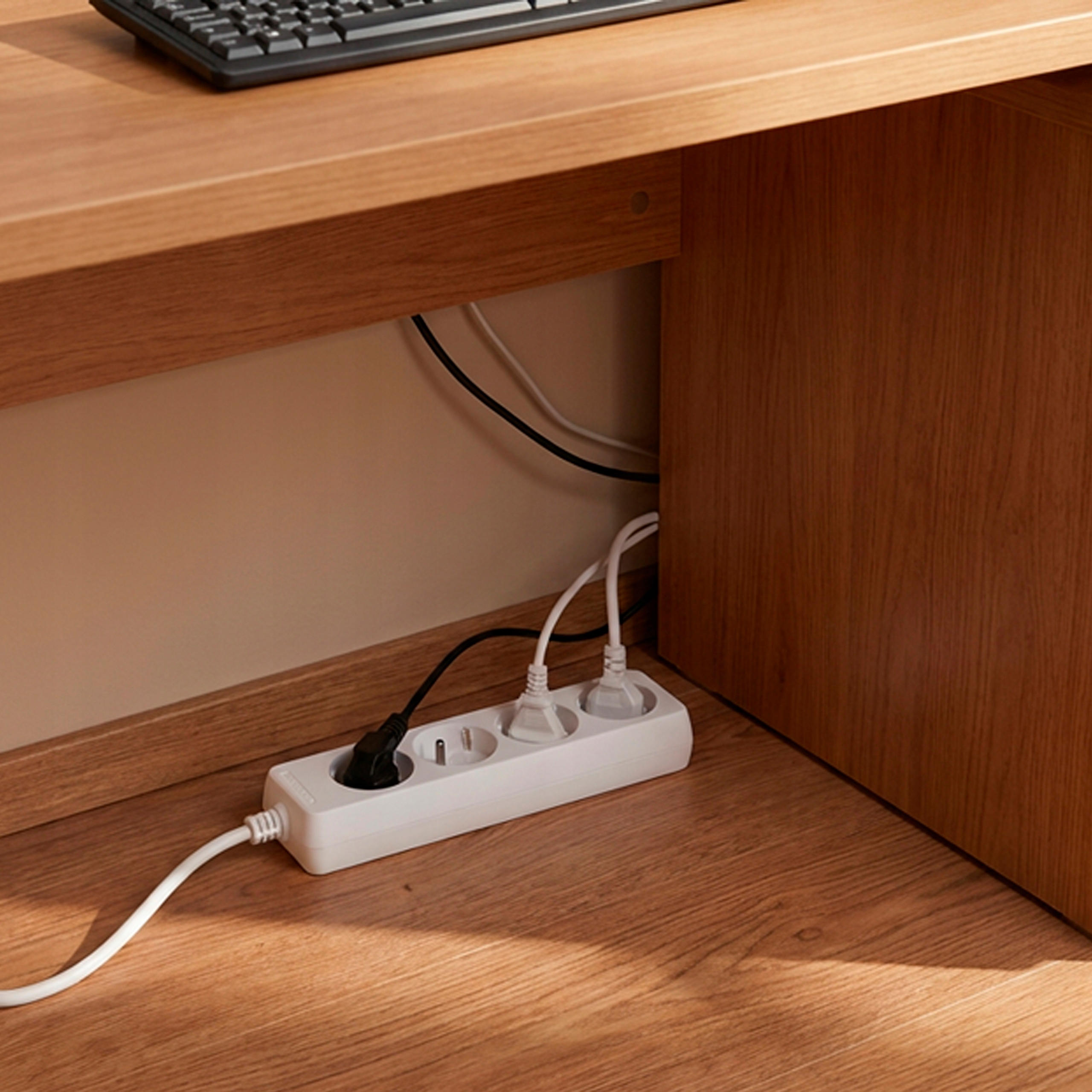 Biała listwa zasilająca z kablami pod biurkiem.