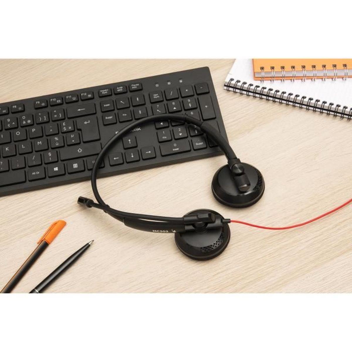 Schwarze Tastatur, Headset mit rotem Kabel und Stifte auf Holztisch.