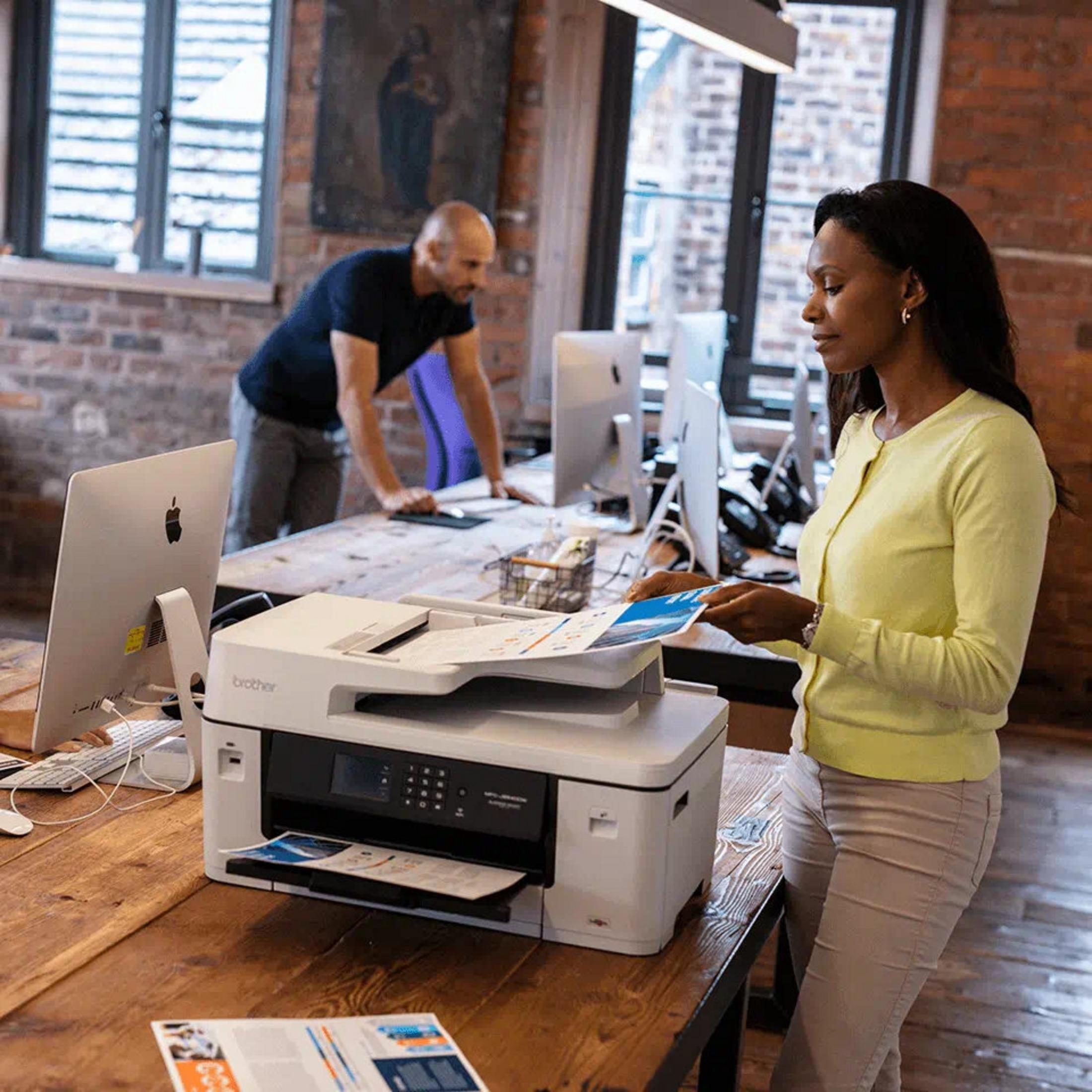 Kobieta wkłada papiery do drukarki, mężczyzna pracuje w tle.
