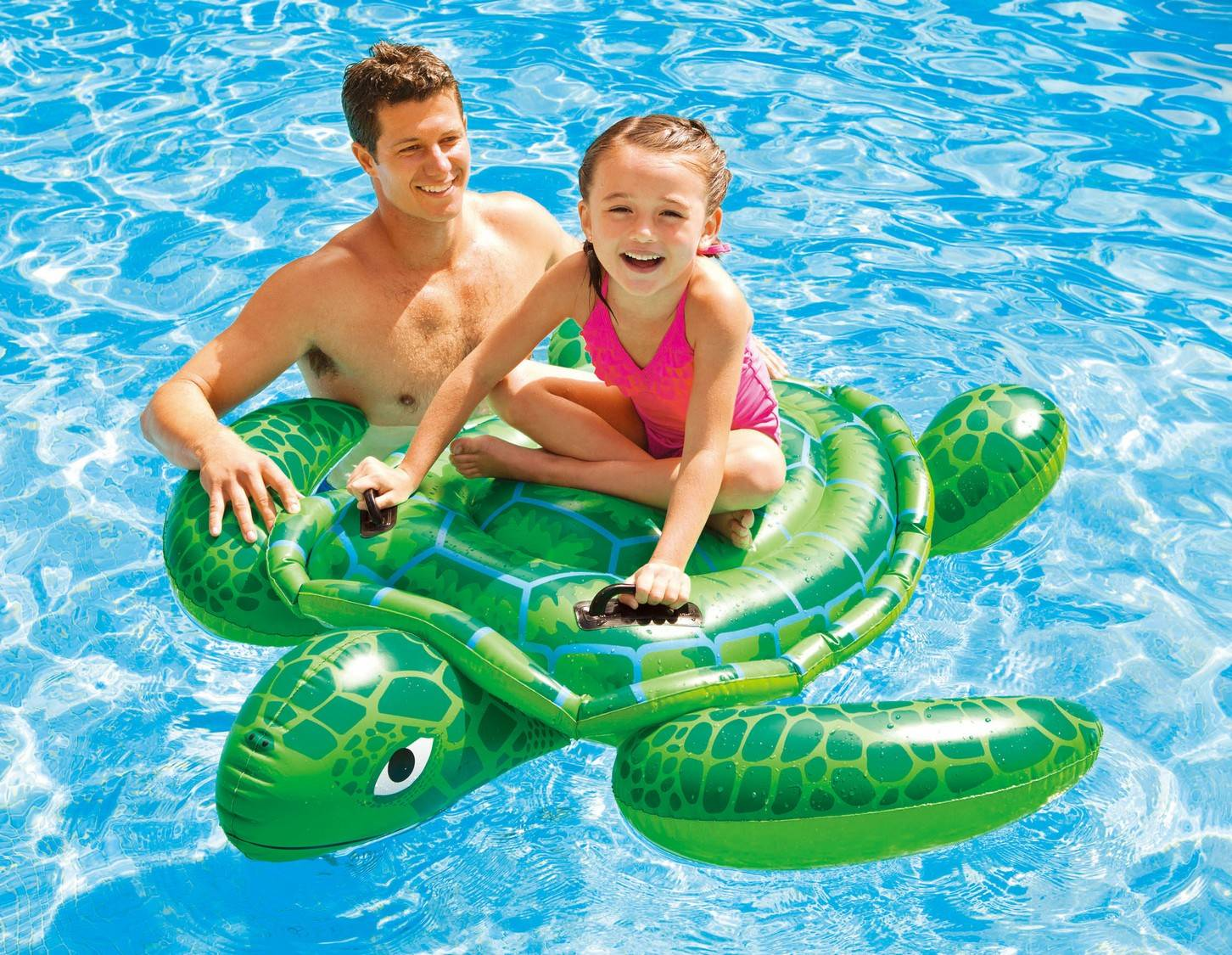 Hombre y niña en flotador de tortuga verde en agua azul.