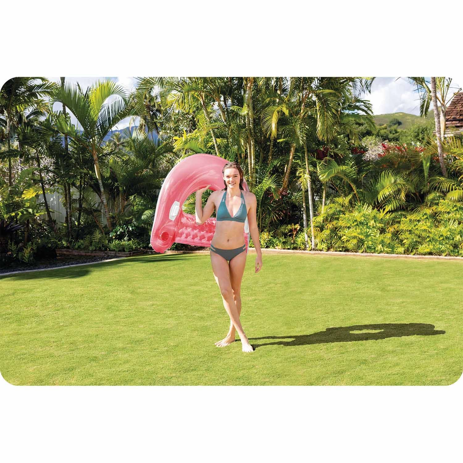 Mujer con flotador inflable rosa de flamenco en patio verde.