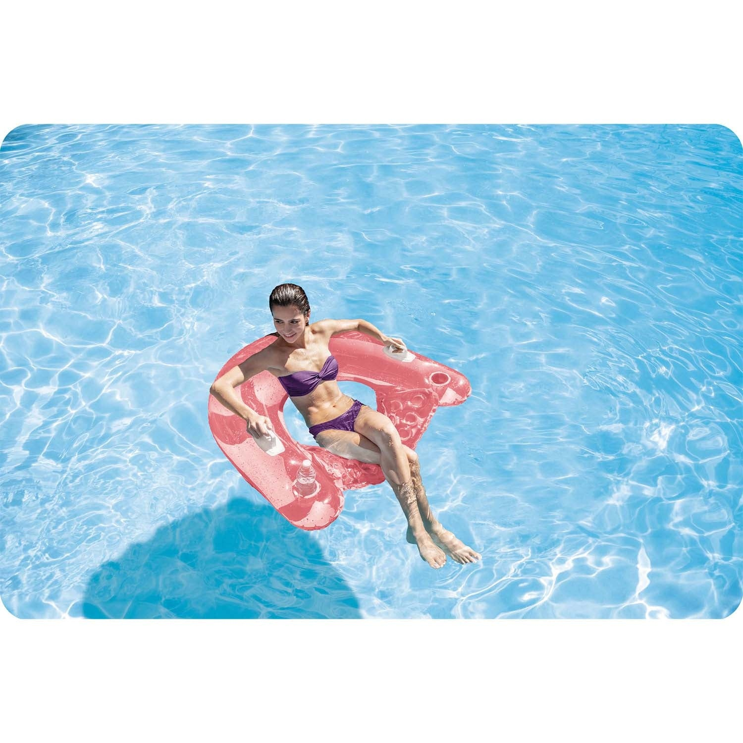Una mujer en bikini morado flota en un flotador rosa en una piscina azul.