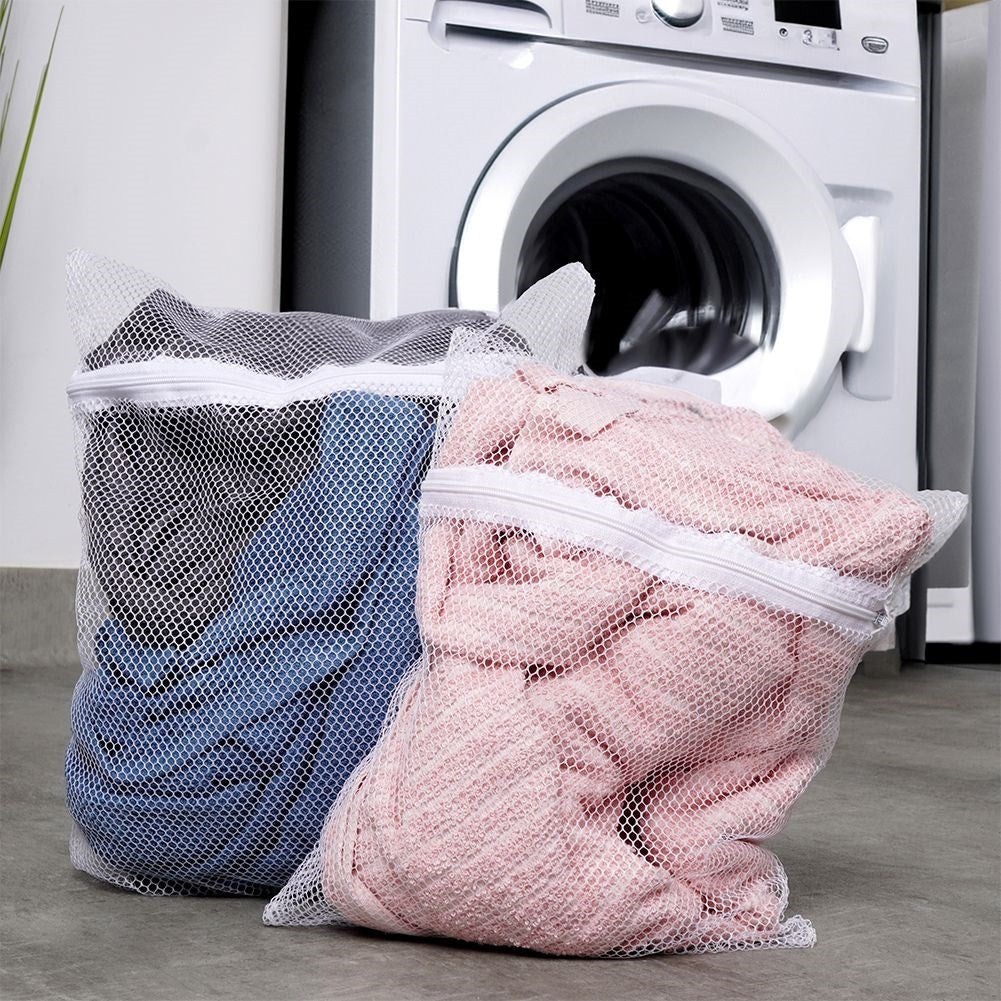 Dos bolsas de malla para ropa, llenas de ropa, están frente a una lavadora.