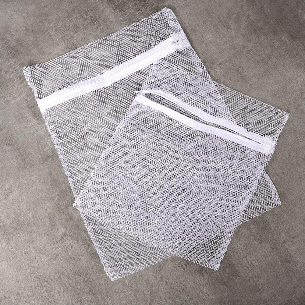 Dos bolsas de malla blanca para la ropa con cremalleras yacen sobre una superficie gris.