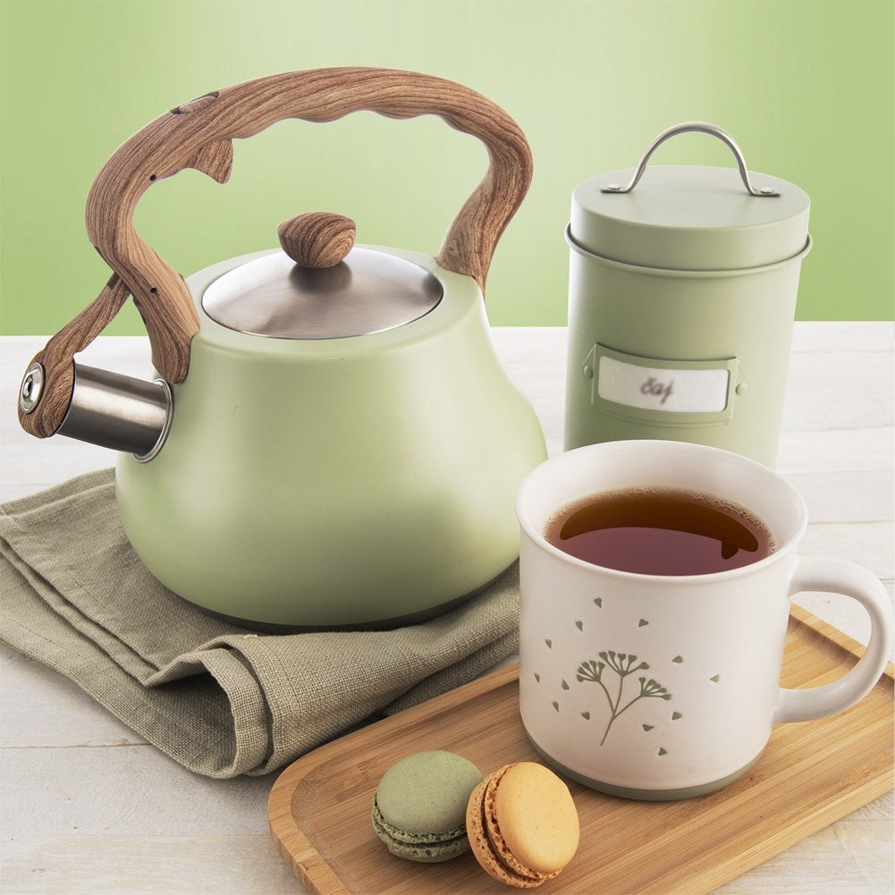 Una tetera verde claro con mango de madera, lata de té, taza de té y dos macarons.