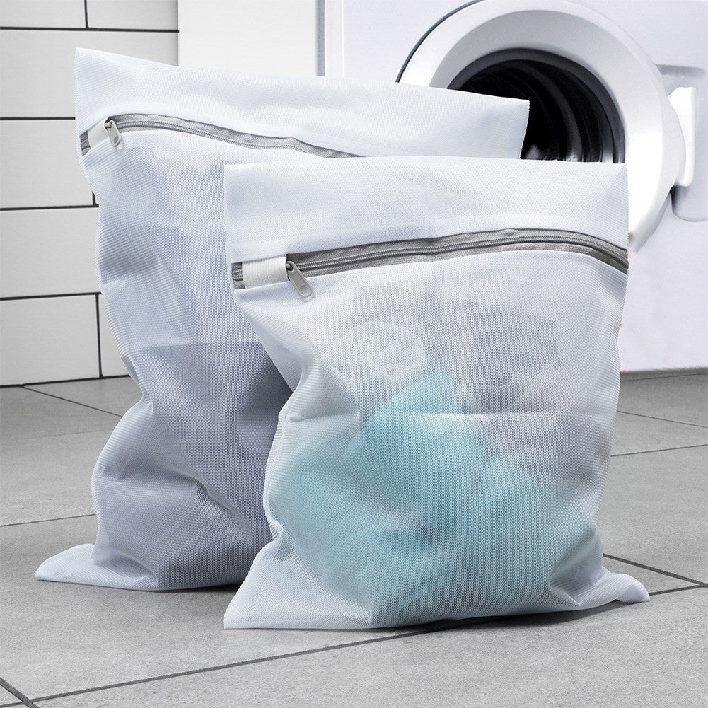 Dos bolsas de lavandería de malla blanca con cremalleras están frente a una lavadora.